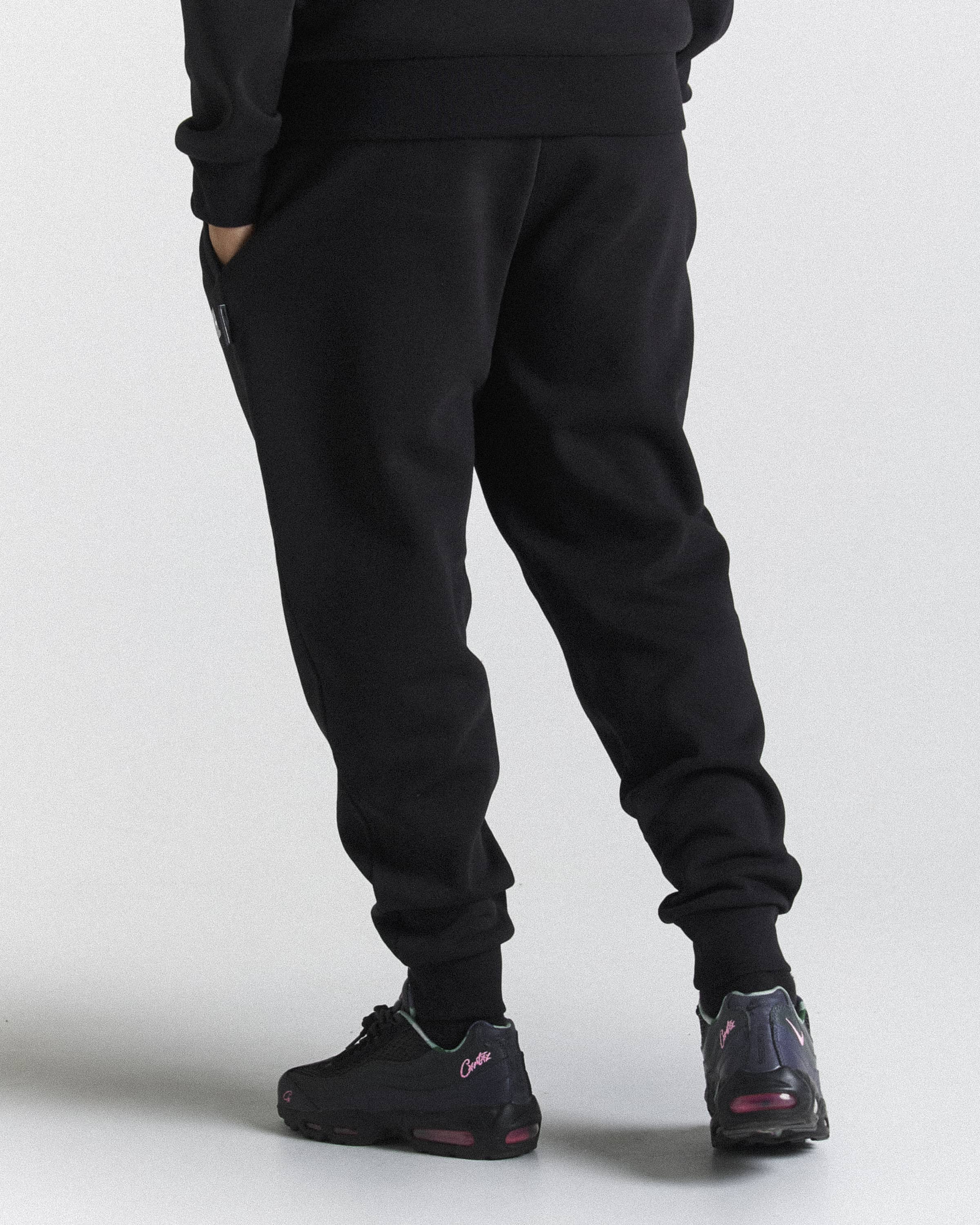 Black jogger sweatpants worn by a model, shown from the back and side against a light gray studio background. The model is also wearing black sneakers.