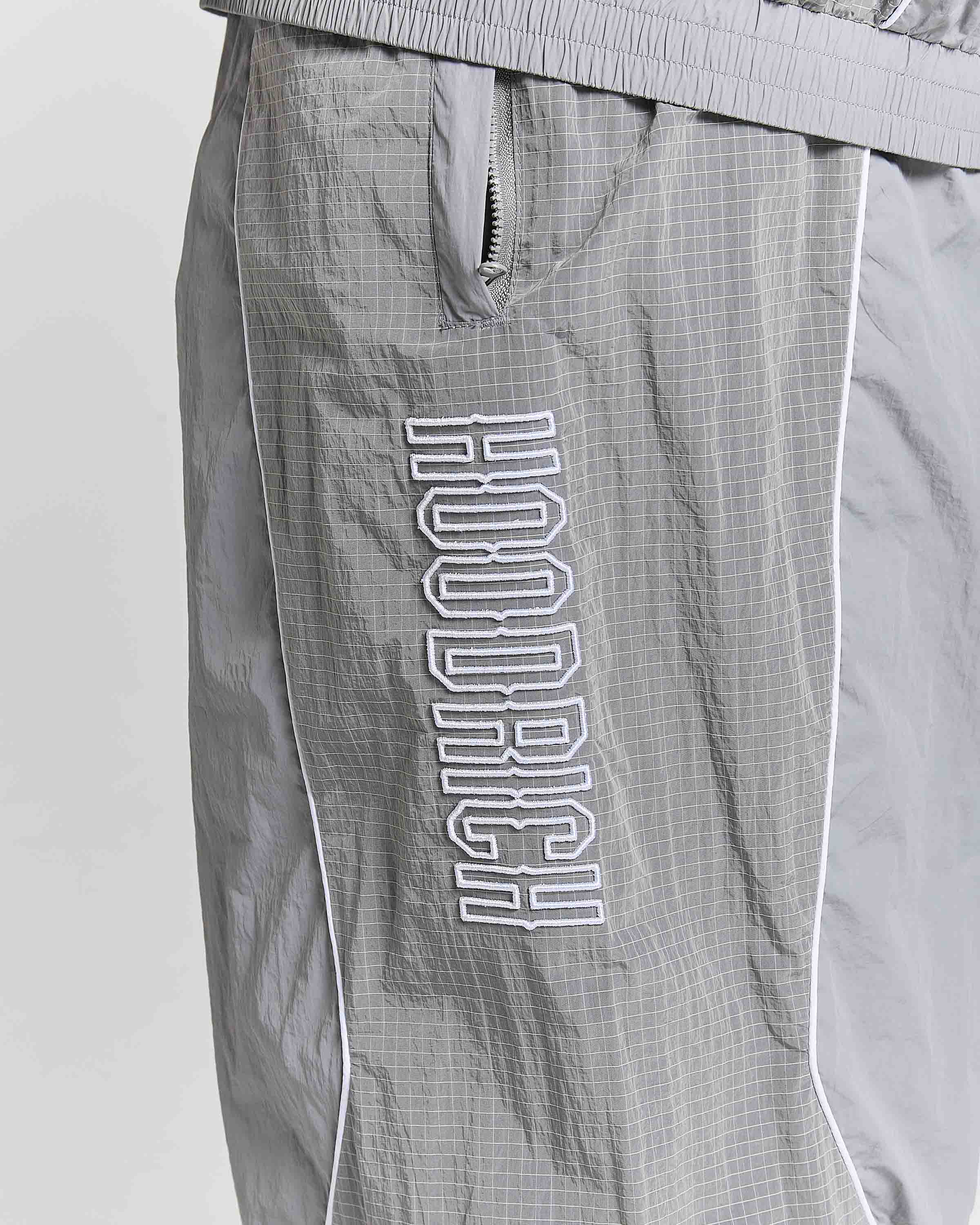 Close-up of gray Hounddog windbreaker shorts with a white outlined vertical logo on the leg, featuring a zippered pocket and white piping.