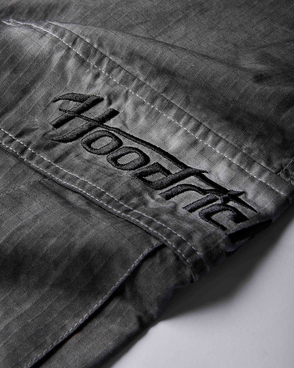 Close-up of dark gray denim fabric with a large embroidered black 'Hoodrich' logo patch on the pocket.