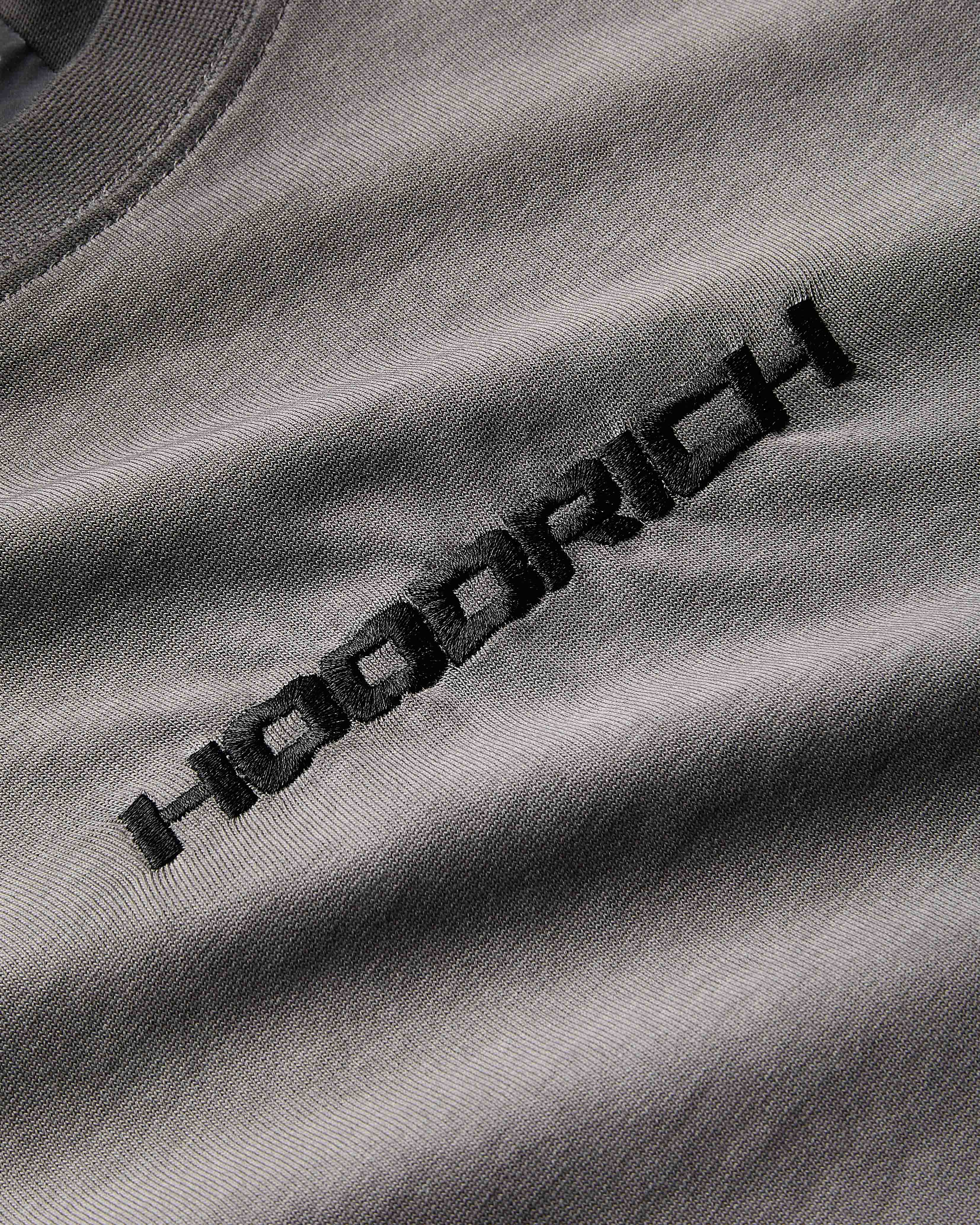 Extreme close-up of the black embroidered Hoodrich logo and textured fabric on an oil wash t-shirt.