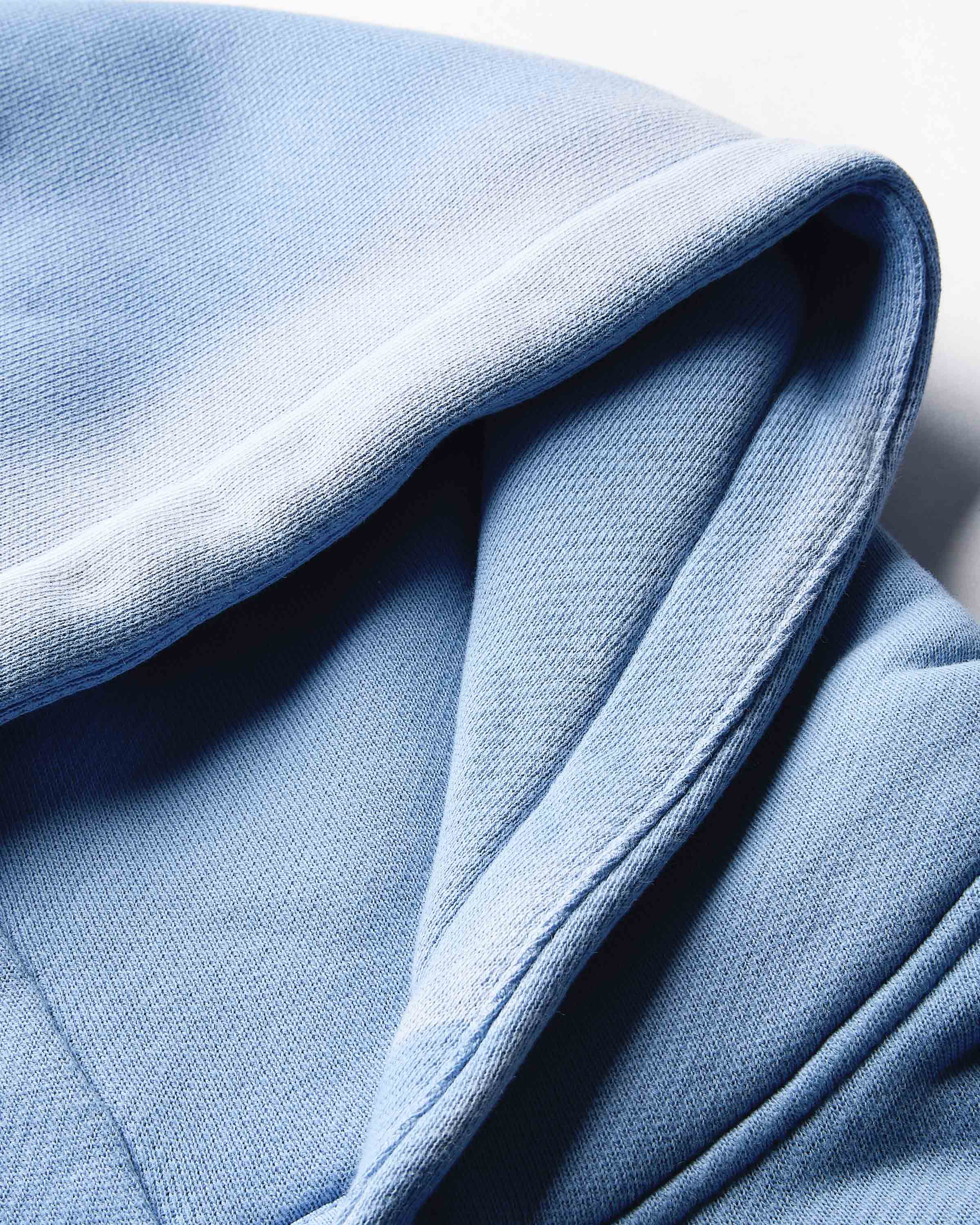 Extreme close-up of the embroidered Hoodrich logo on the blue fabric of the hoodie.