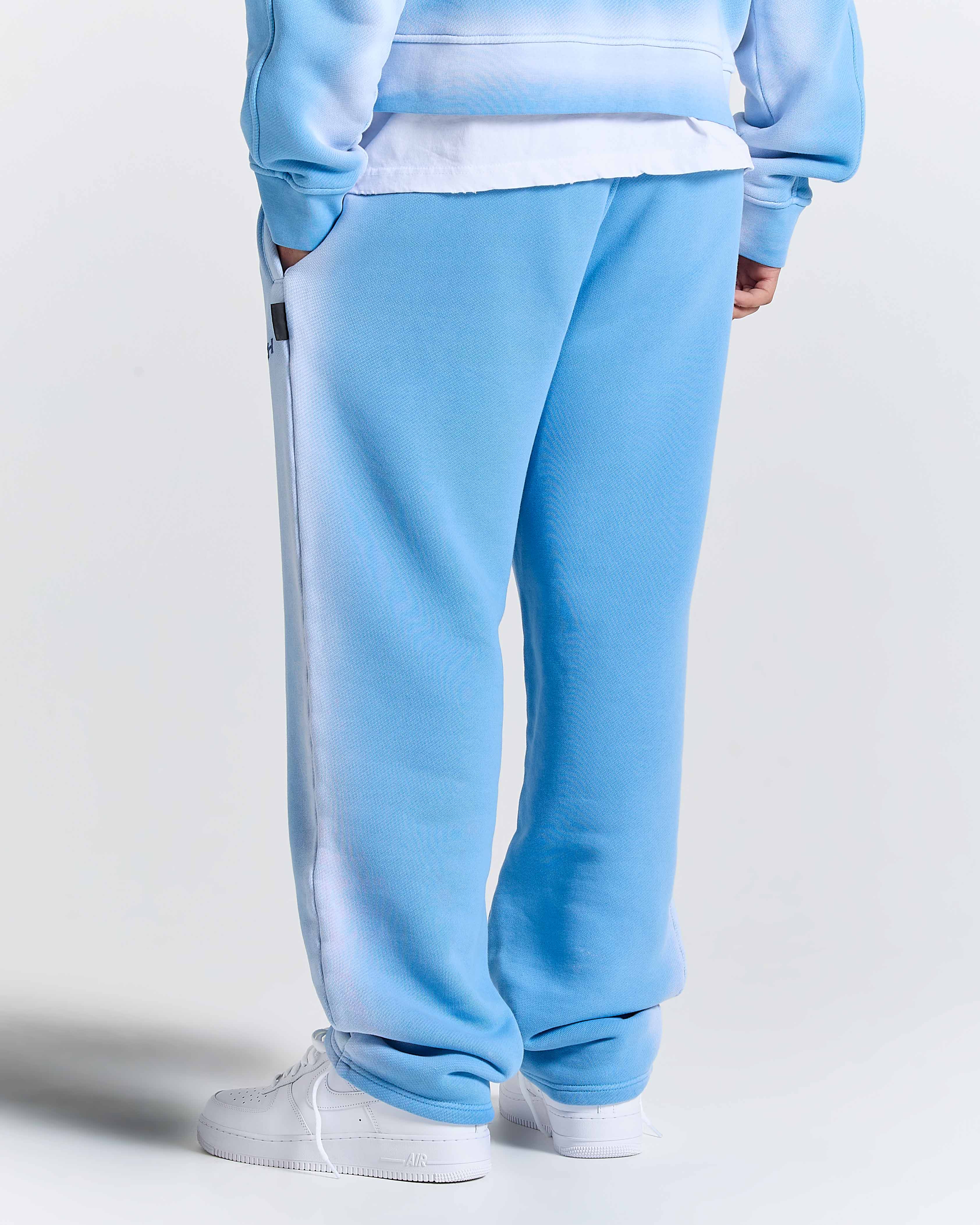 Model seen from behind wearing oversized blue joggers, white socks, and white trainers.