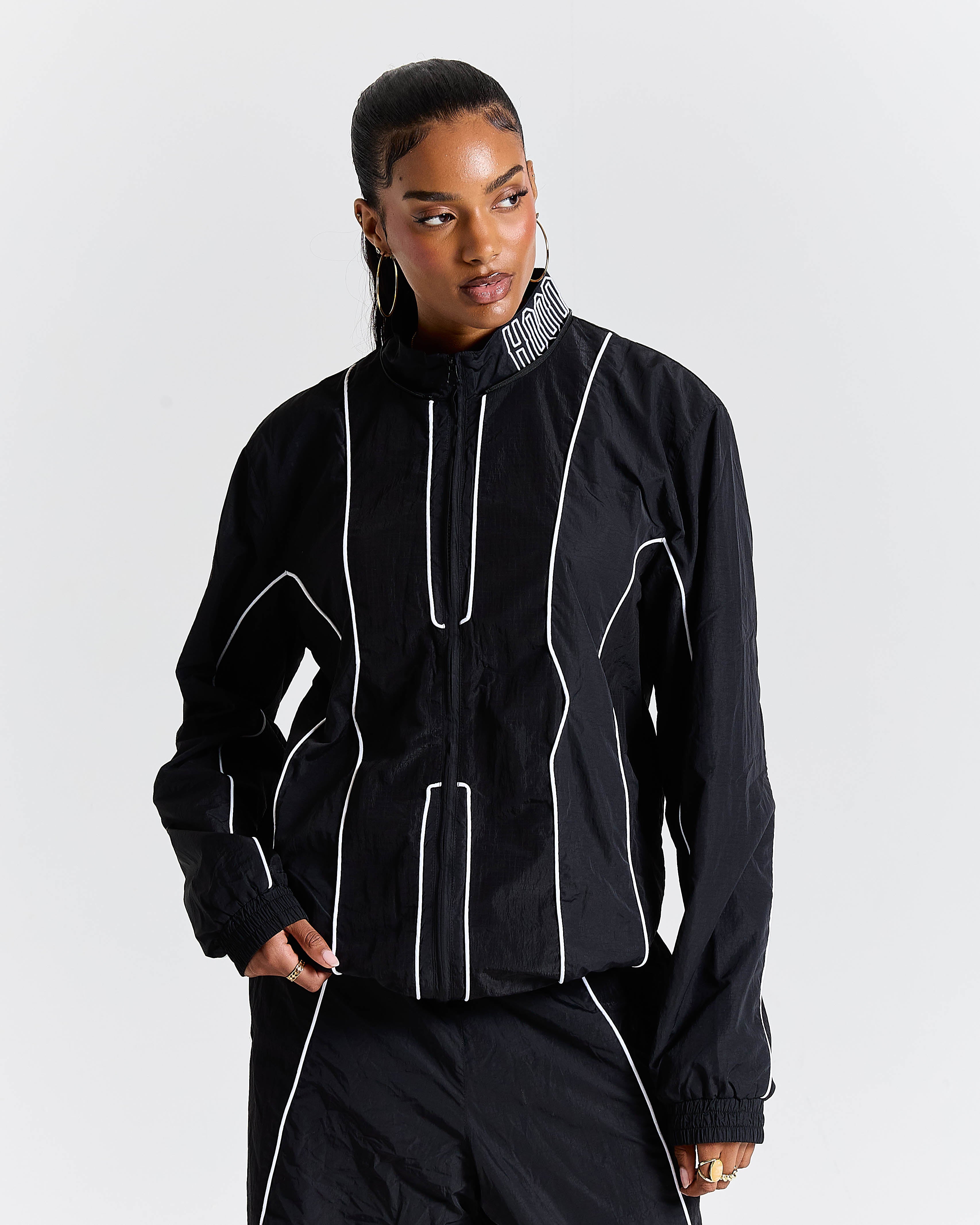 Person wearing a black outfit with white piping on a plain background