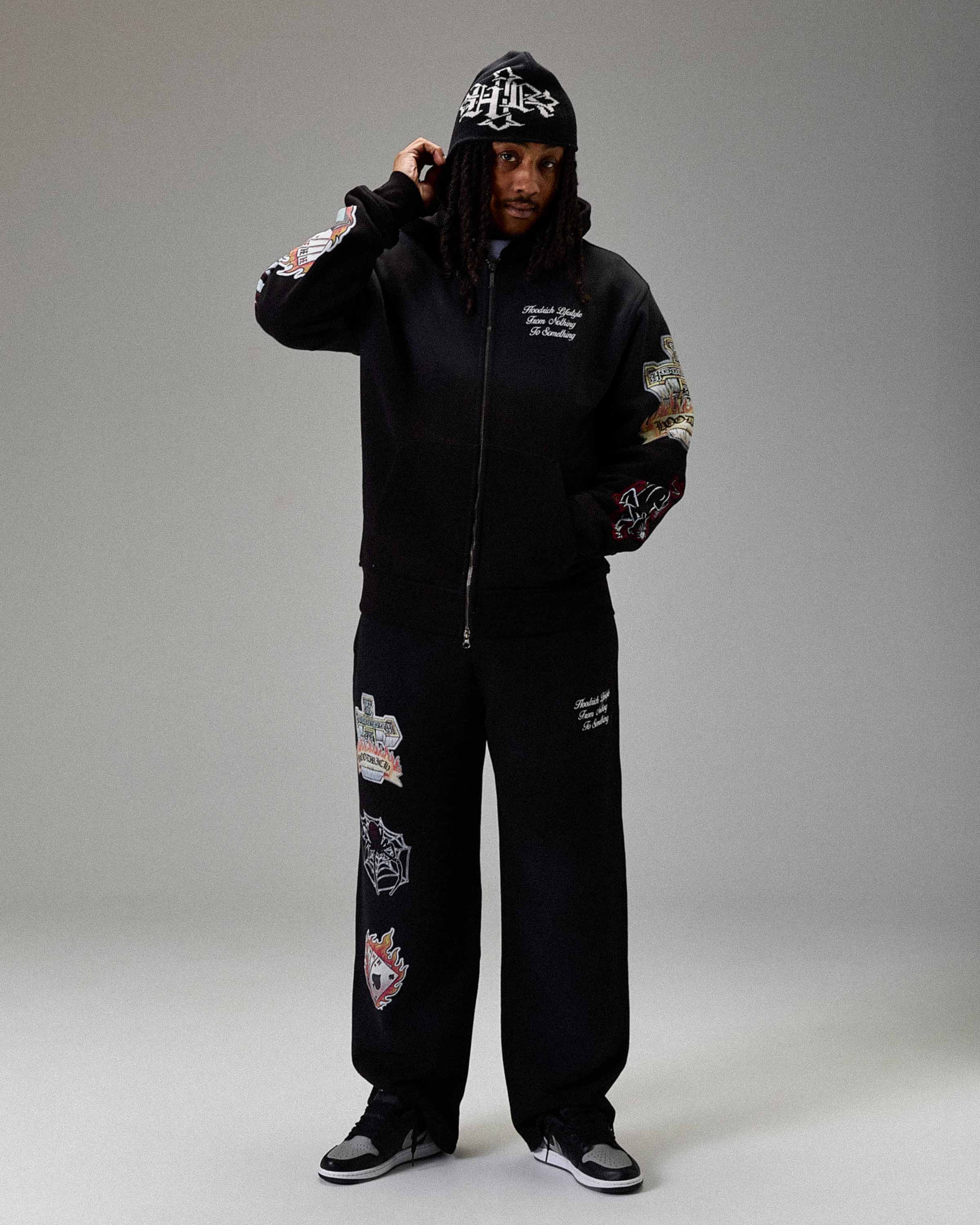 Displays a model wearing the Black 'Hoodrich' branded men's The Winner's Circle Phase Full Tracksuit