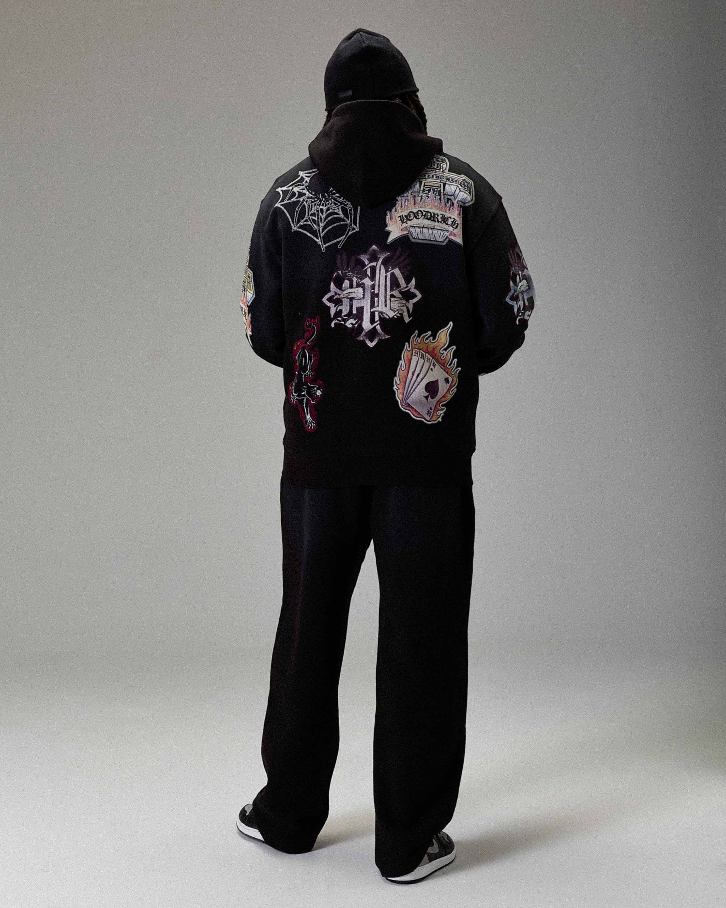 Person wearing a black hoodie with various designs on a gray background