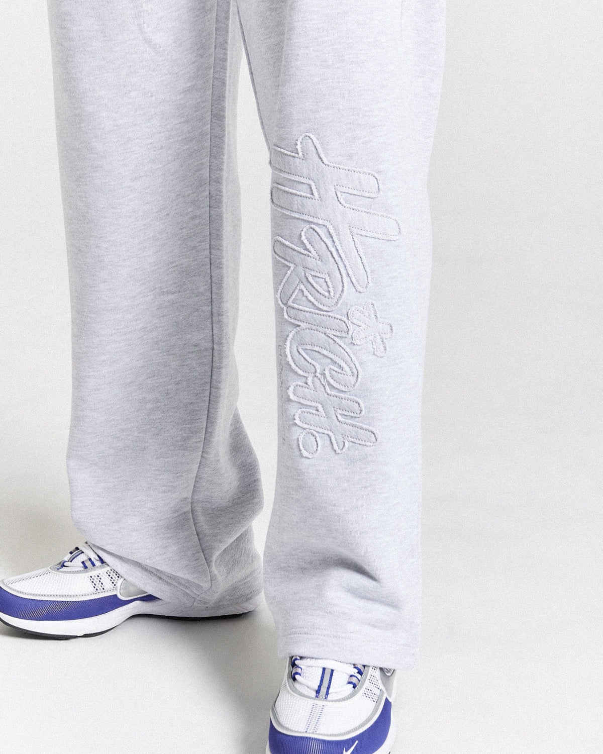Displays a model wearing the light grey 'Hoodrich' branded men's Asthrich Full Tracksuit featuring the details on the branding
