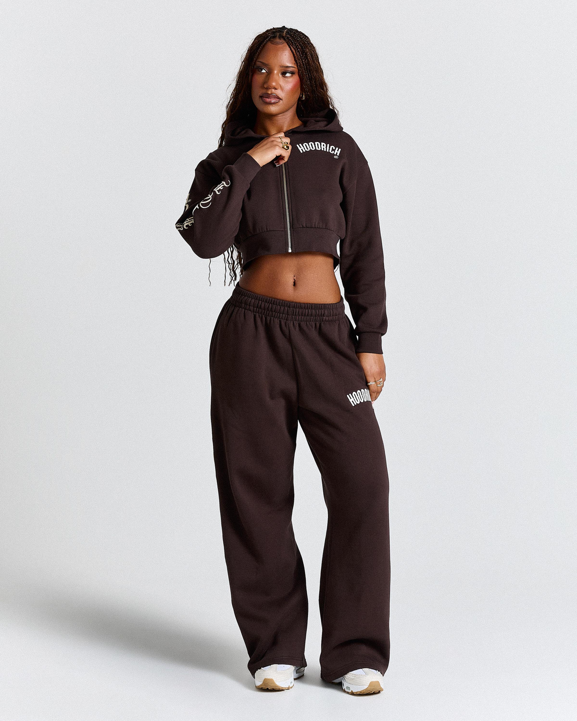 Woman wearing a brown tracksuit with visible branding on a white background