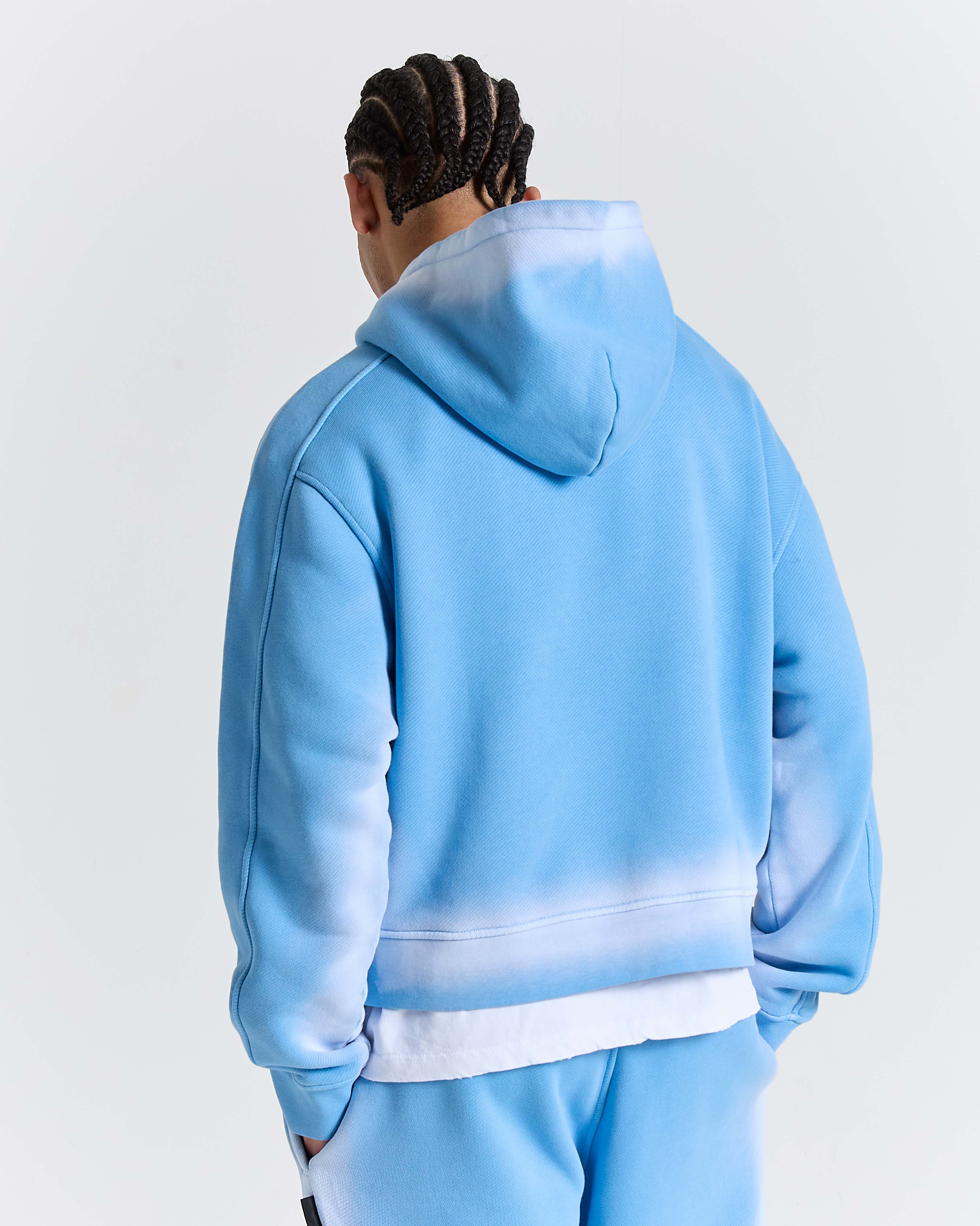 Back view of male model wearing a light blue hoodie and pants on a white background