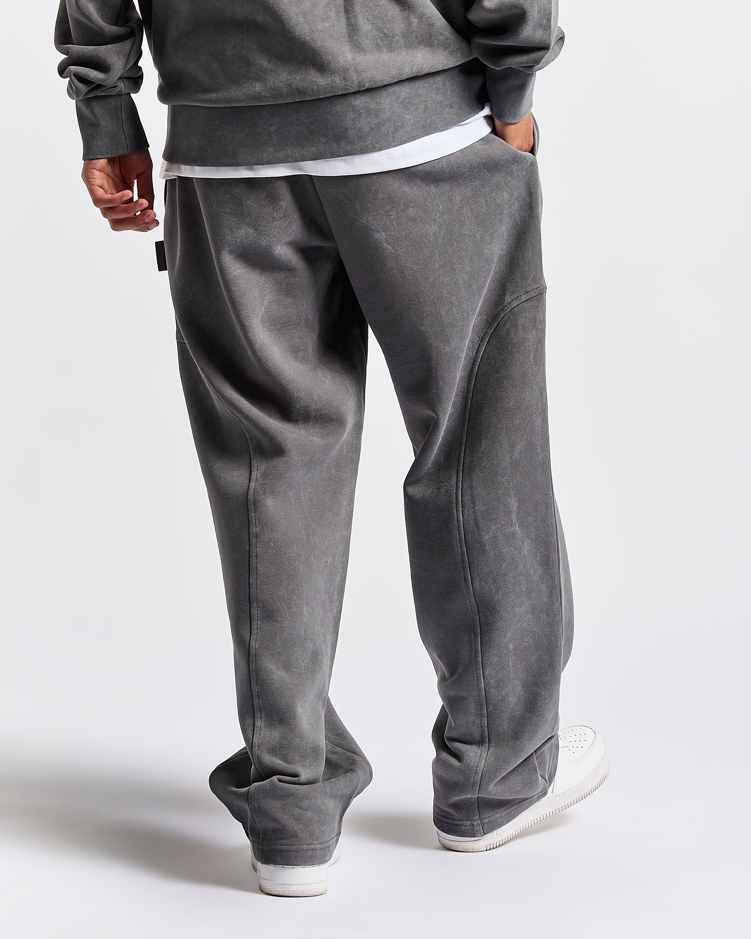 A person shown from the back wearing loose-fit gray sweatpants, a gray sweatshirt, and white sneakers against a clean light gray studio background.