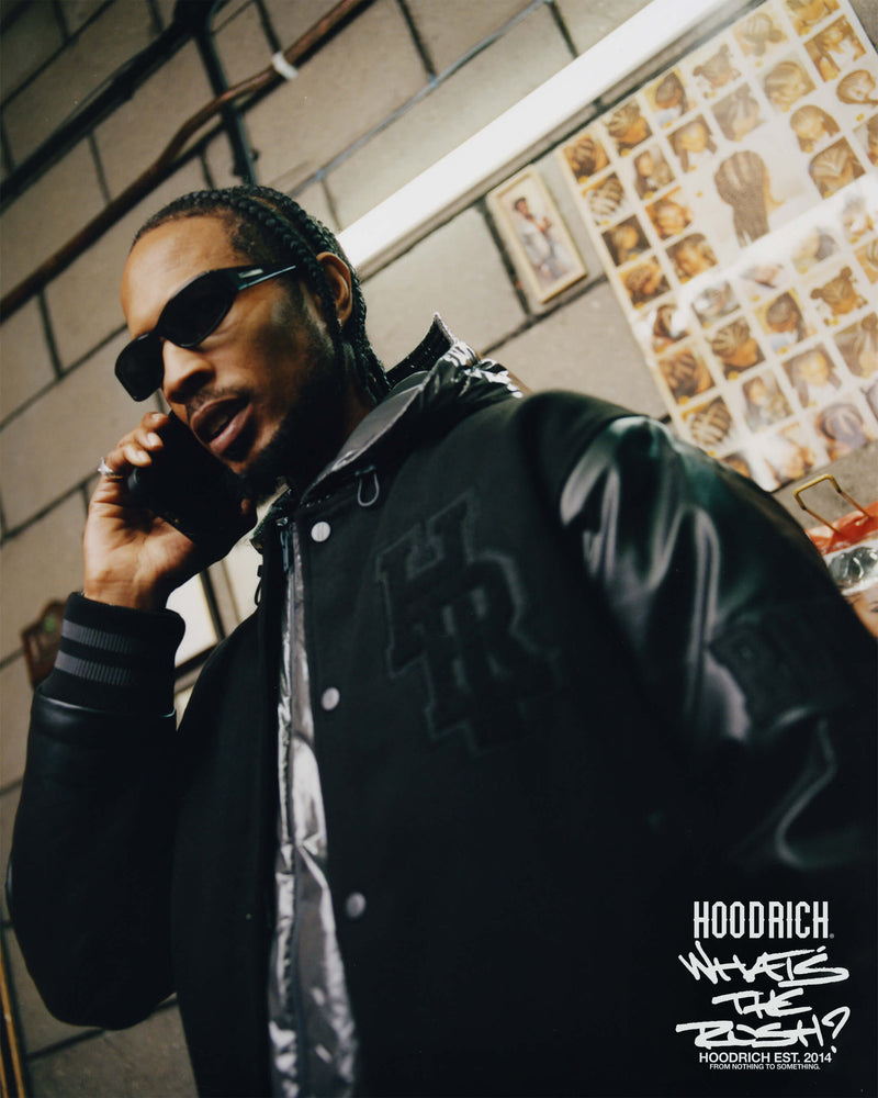 Man in a black jacket with a brand logo, talking on a phone in an indoor setting.
