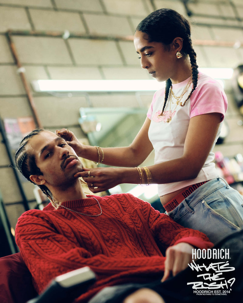 A man getting his haircut by a female barber with 'Hoodrich' branding in the corner of the image.