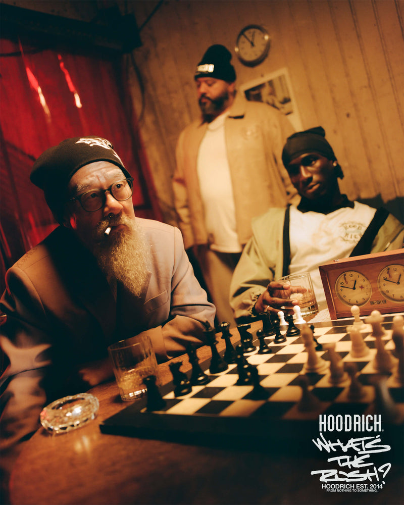Three men playing chess in a dimly lit room with 'Hoodrich' branding.