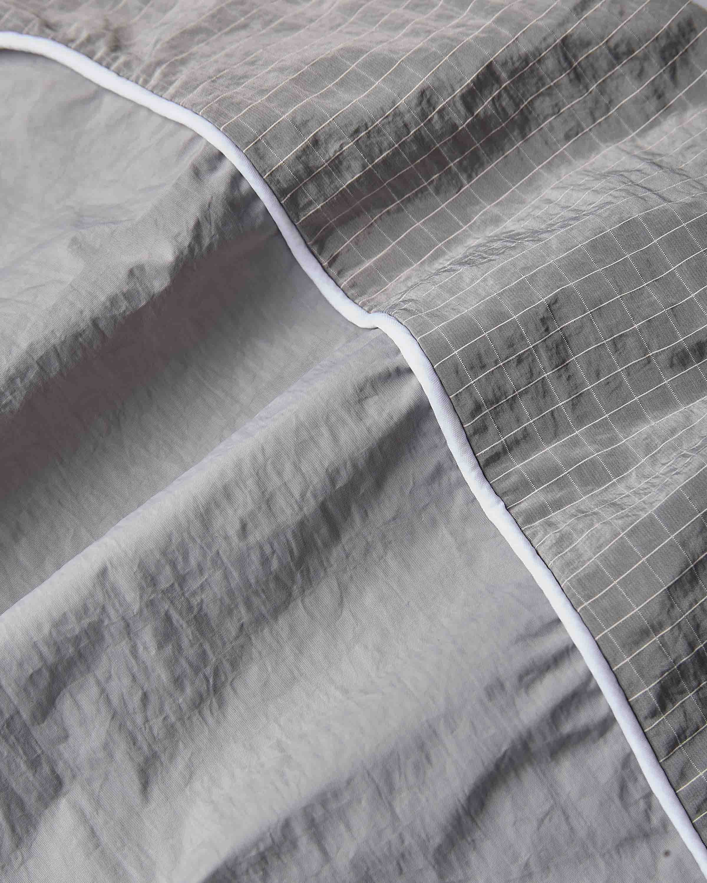 Close-up of a gray quilted fabric with a subtle grid pattern and a contrasting white piping border.