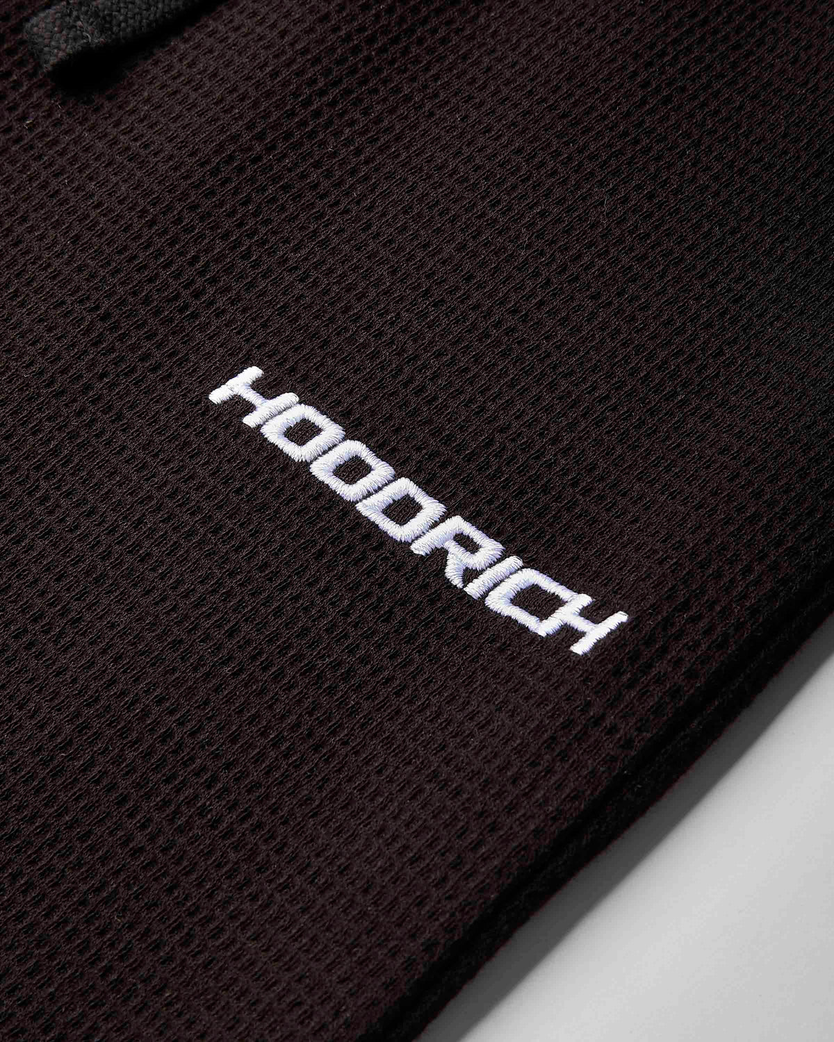 Close-up of a black textured mesh fabric with the brand name 'HOODRICH' printed in white across the center.