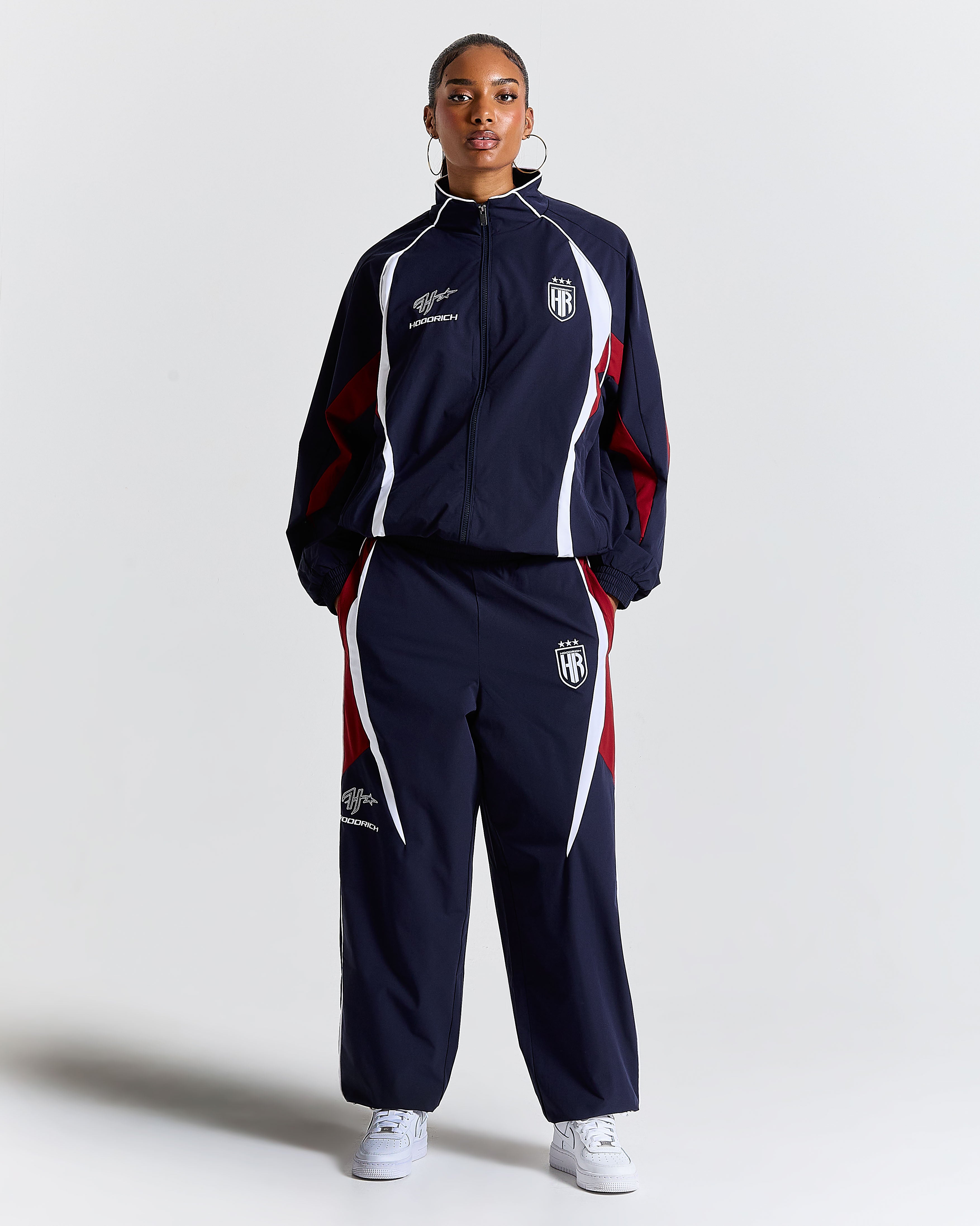 Person wearing a navy tracksuit with red and white accents on a light gray background