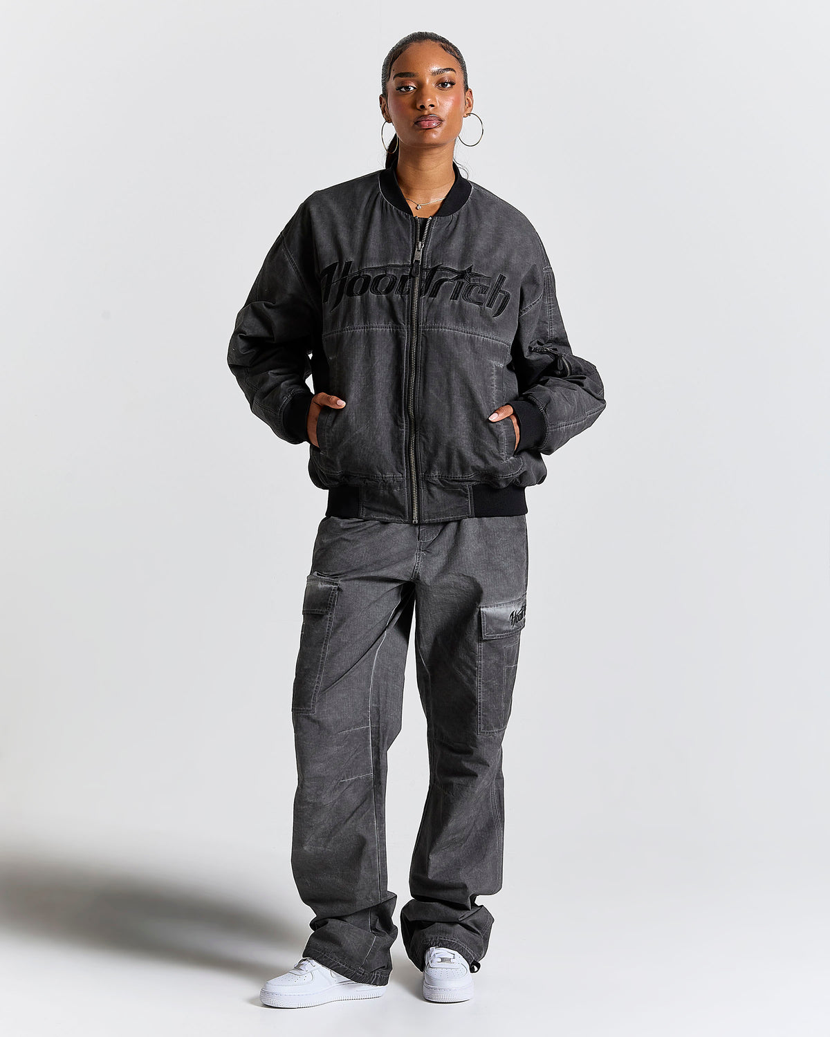 Person wearing a dark gray bomber jacket and pants with 'Hoodrich' branding on a light gray background