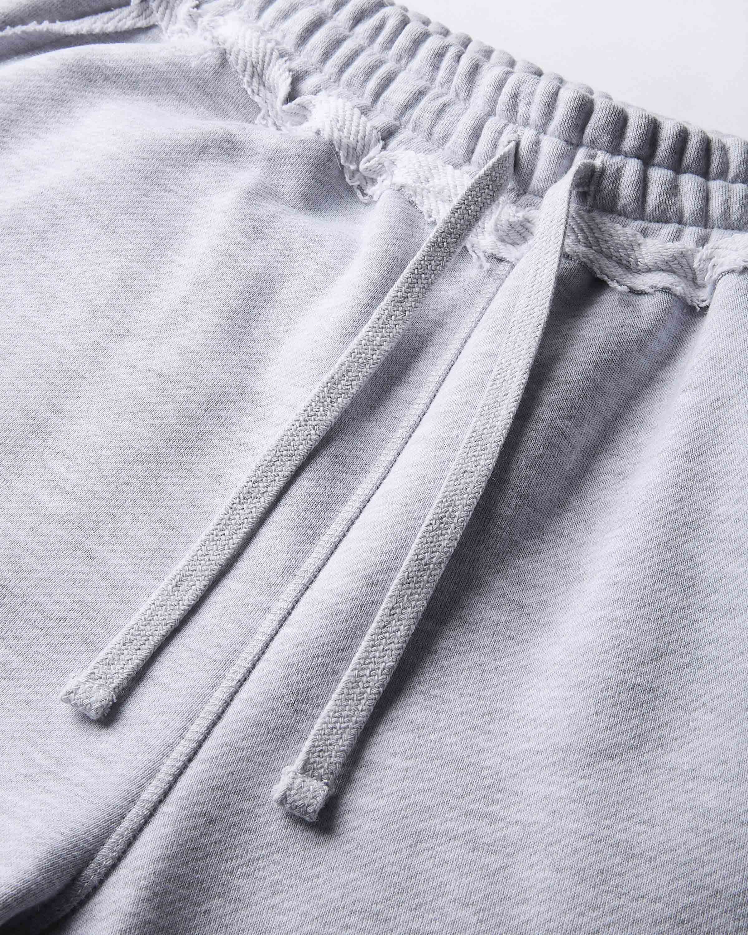 Close-up of light gray heather sweatpants showing the textured fabric, drawstring, and frayed elastic waistband.