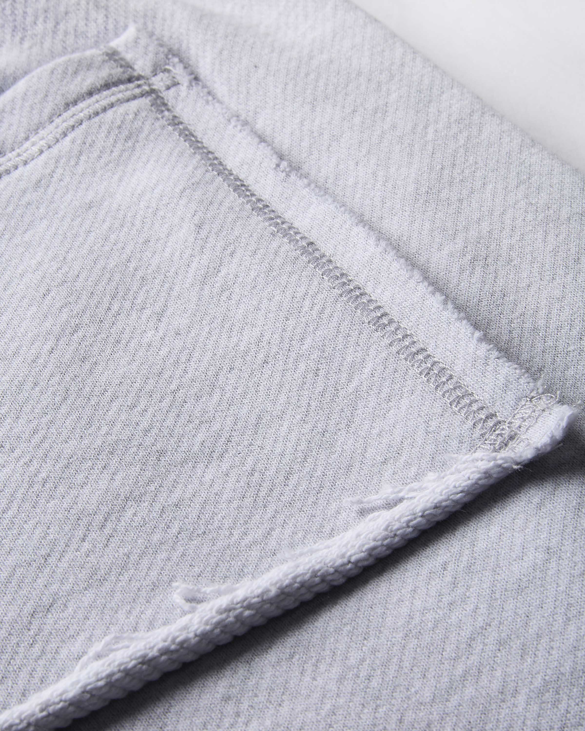 Close-up of light gray tracksuit bottoms showing a folded corner with raw, frayed hems and a stitched seam.