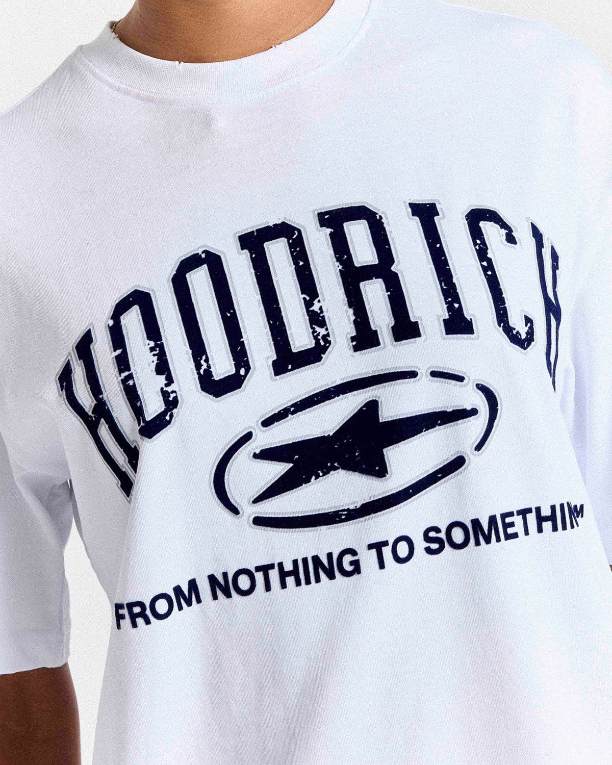 White crewneck t-shirt featuring a distressed navy blue graphic print with the text 'HOODRICH' and 'FROM NOTHING TO SOMETHING' surrounding a star logo.
