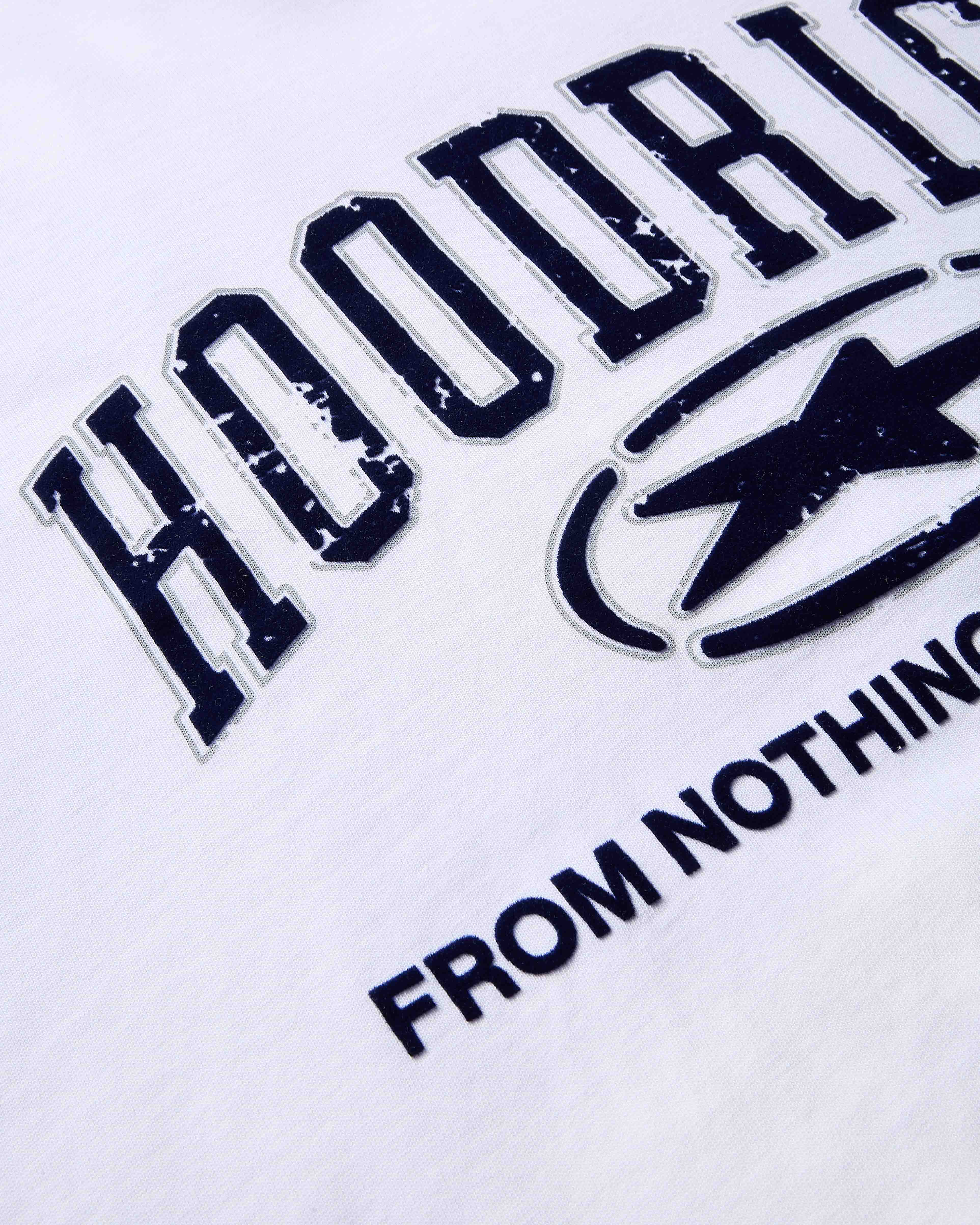 Close-up of dark blue, distressed-effect varsity-style Hoodrich branding and the words 'From Nothing' on a white t-shirt.
