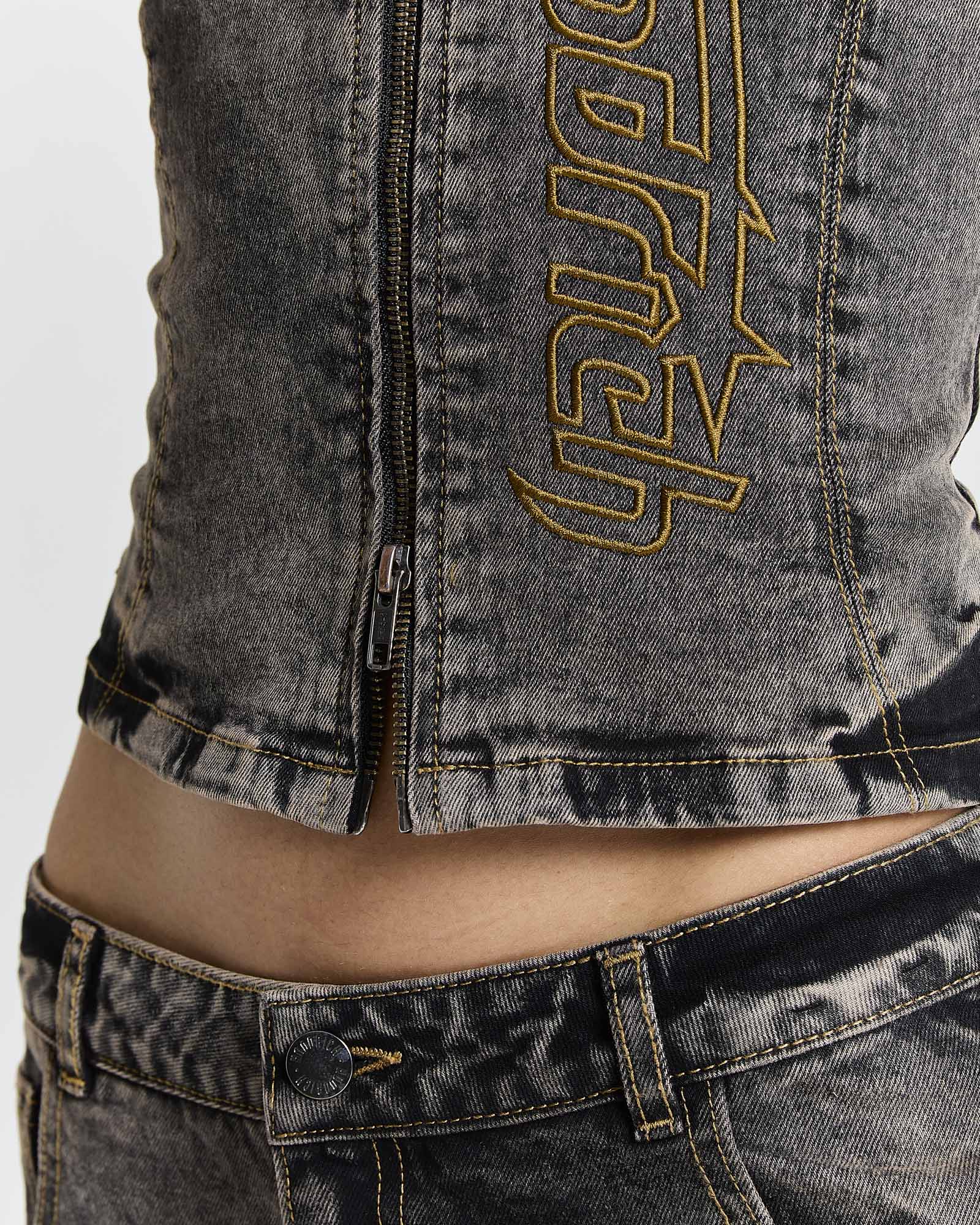 Close-up of the zip hem and yellow Hoodrich logo embroidery on a model wearing a fitted black denim corset top.