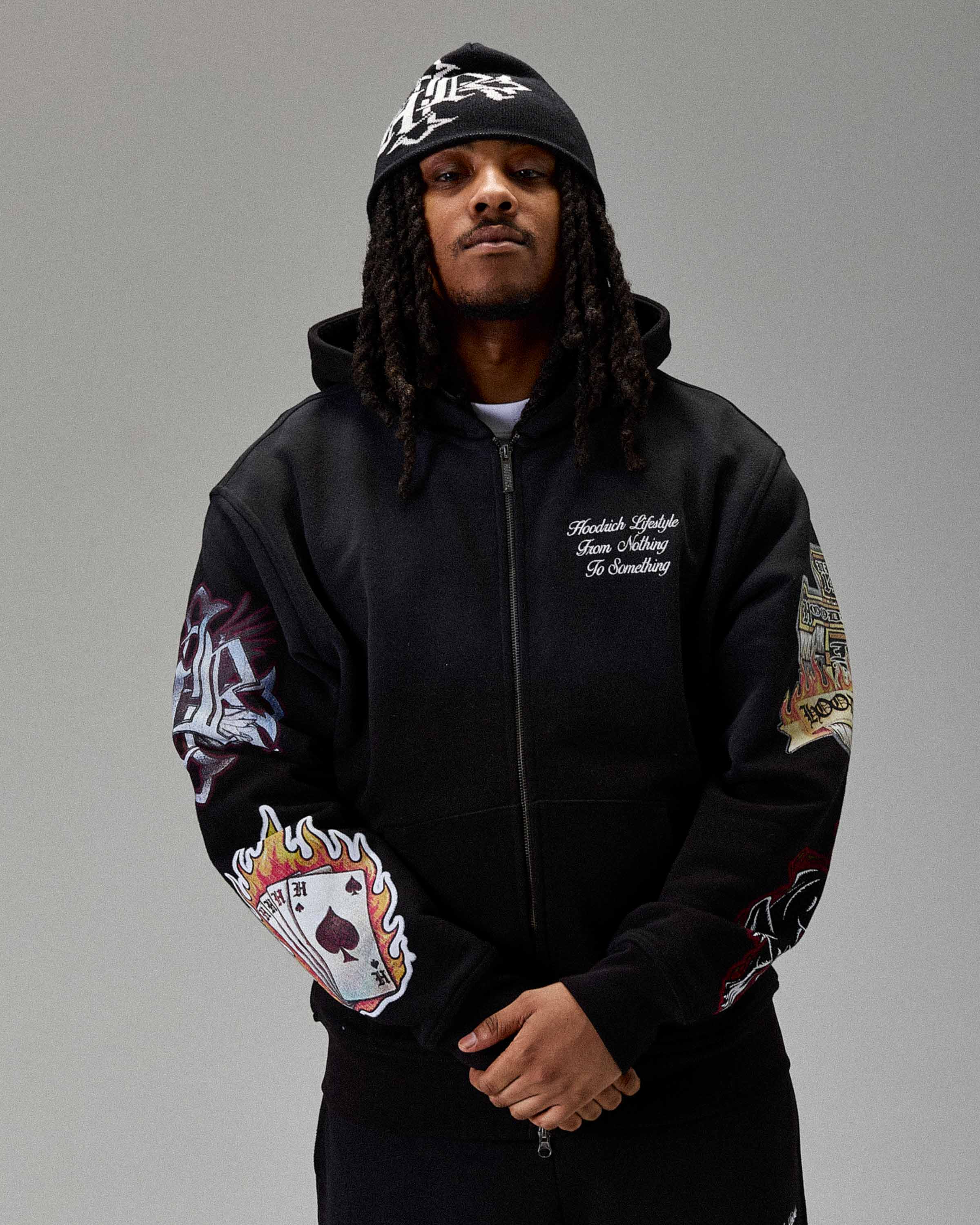 Person wearing a black hoodie with colorful designs on sleeves against a gray background