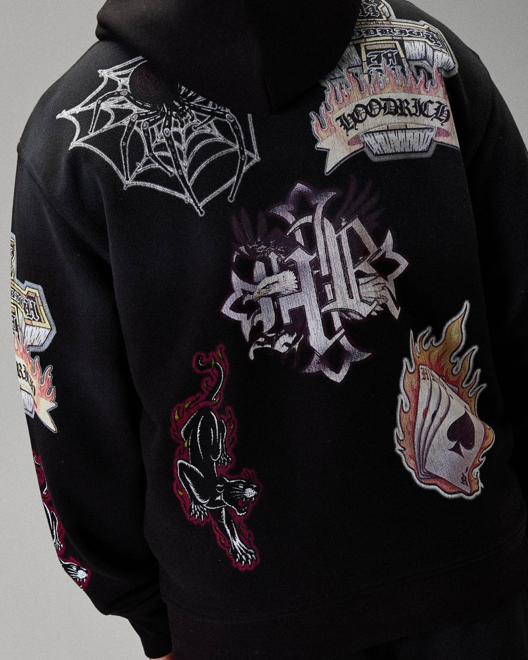 Black hoodie with various intricate designs and logos on a gray background