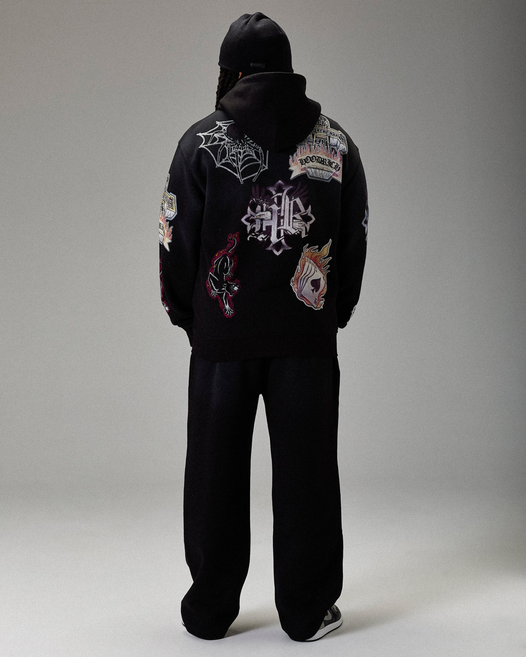 Person wearing a black hoodie with various designs on the back against a gray background