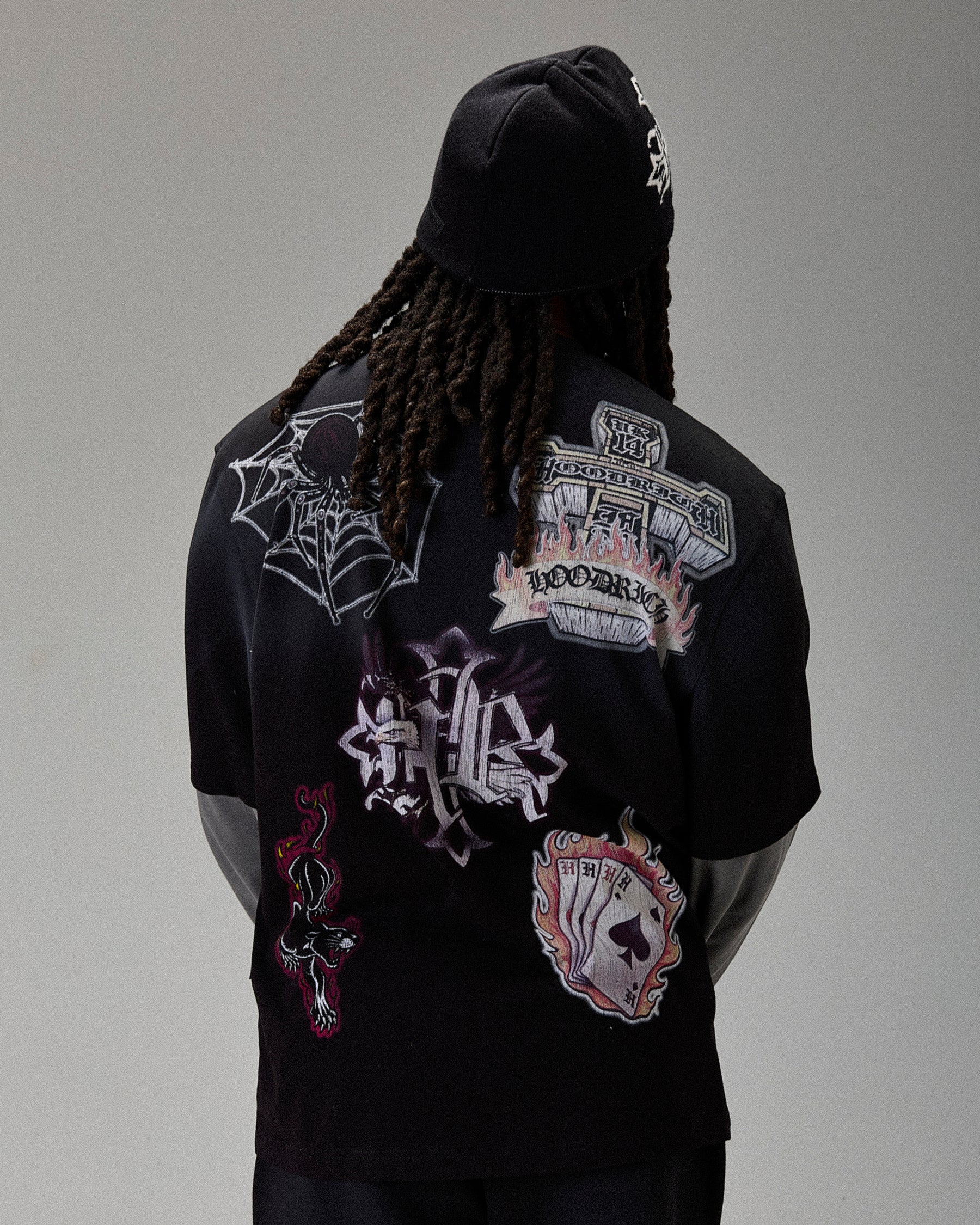 Person wearing a black hoodie with various patches on the back against a gray background