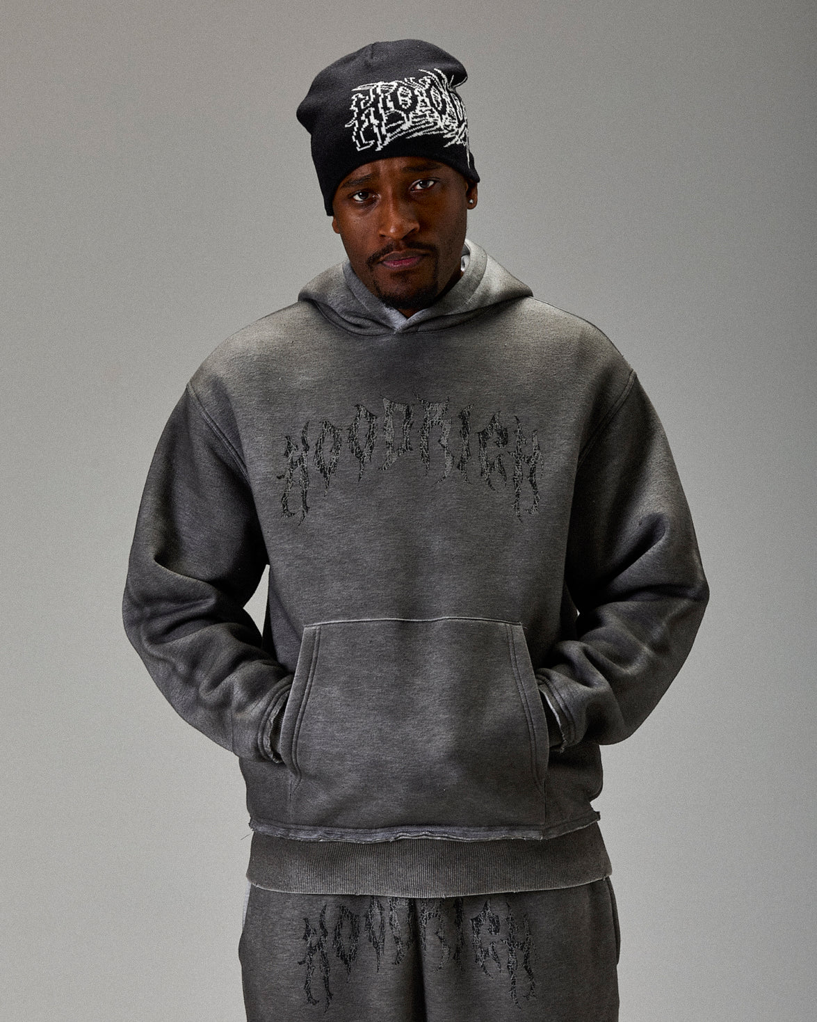 Person wearing a gray hoodie and pants with text, standing against a plain background