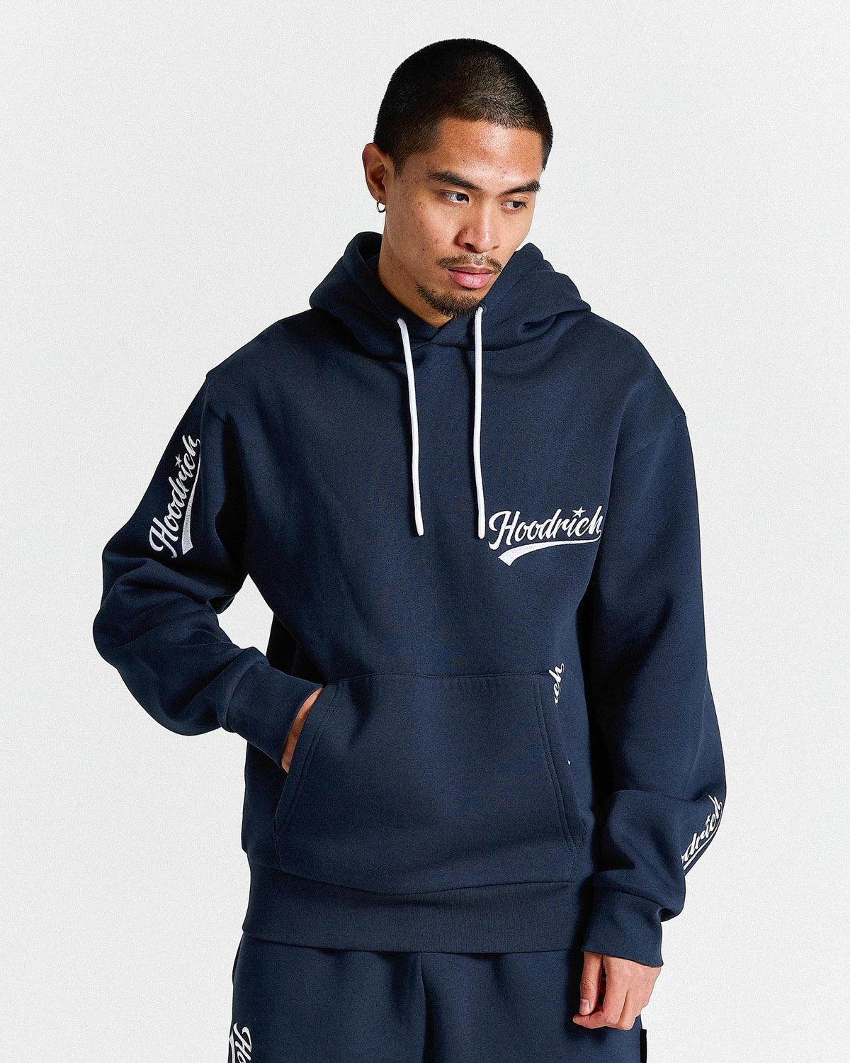 Man wearing a navy blue hoodie with 'Hoodrich' branding on a light gray background