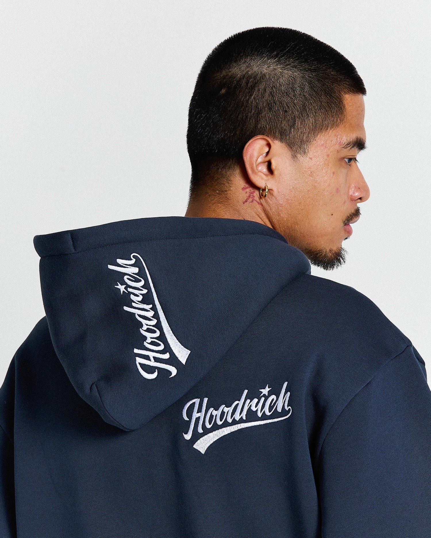 Person wearing a navy blue hoodie with 'Hoodrich' branding on the back against a light gray background