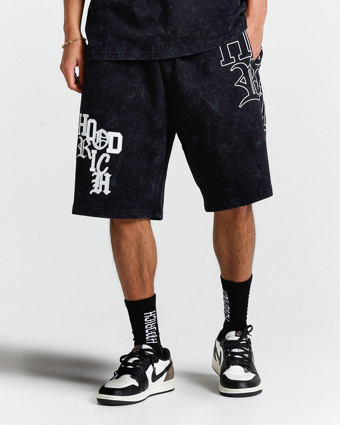 Person wearing black shorts with white text and black sneakers on a white background