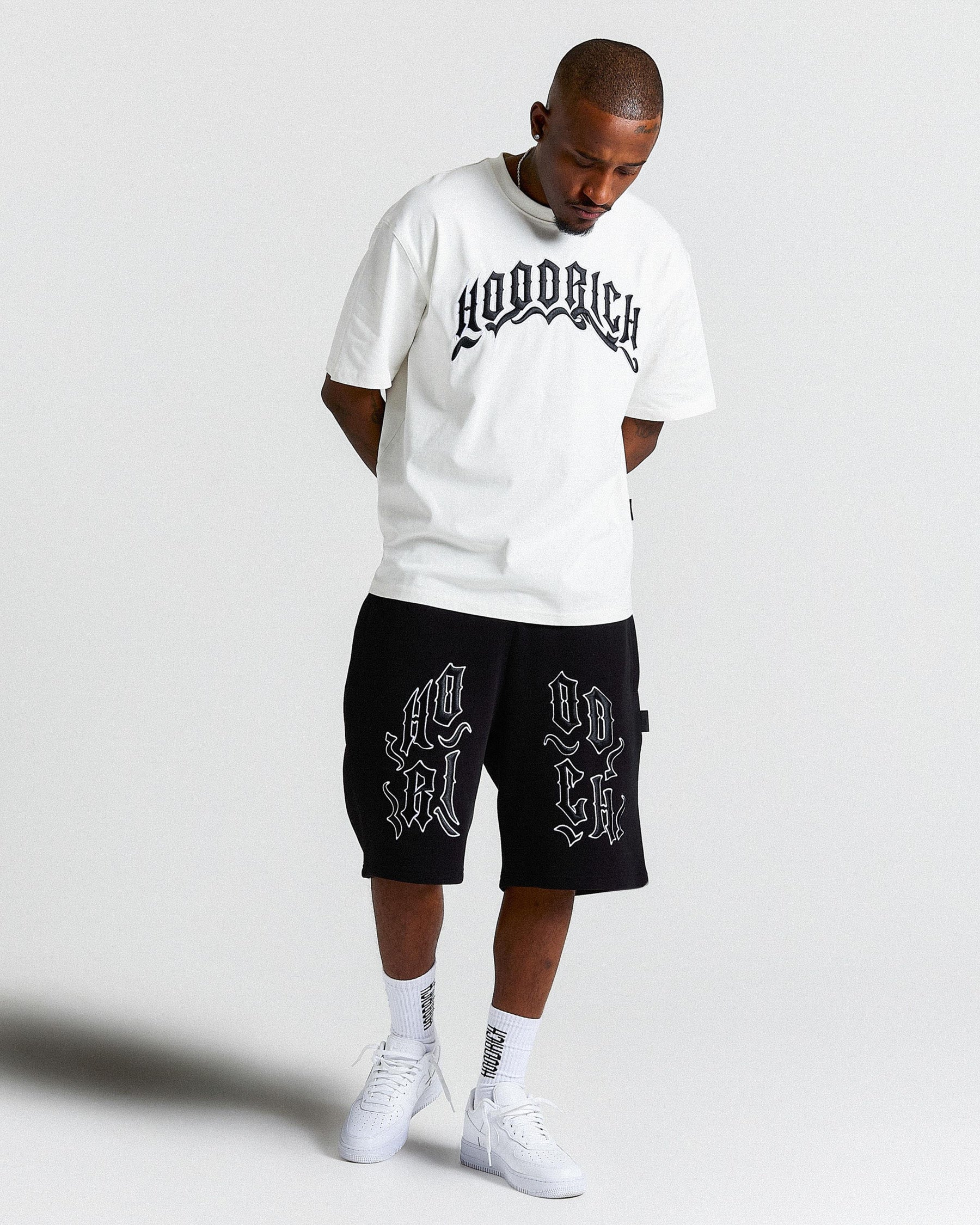 Man wearing a white t-shirt and black shorts with 'Hoodrich' branding on a light gray background