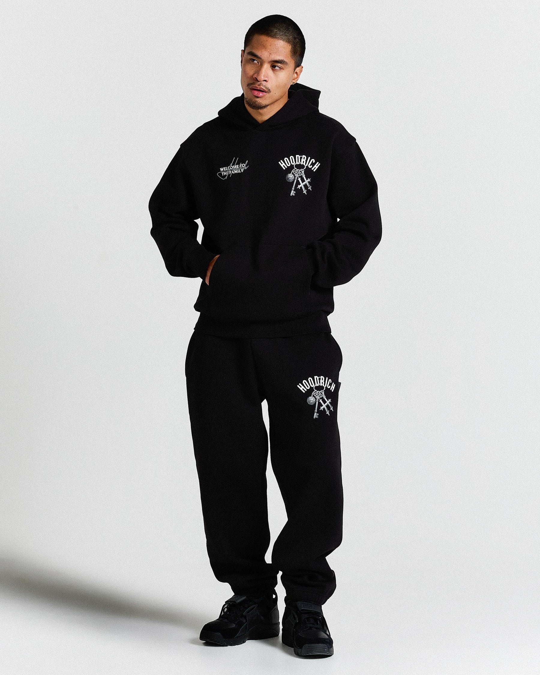 Person wearing a black hoodie and sweatpants set with visible branding on a light gray background