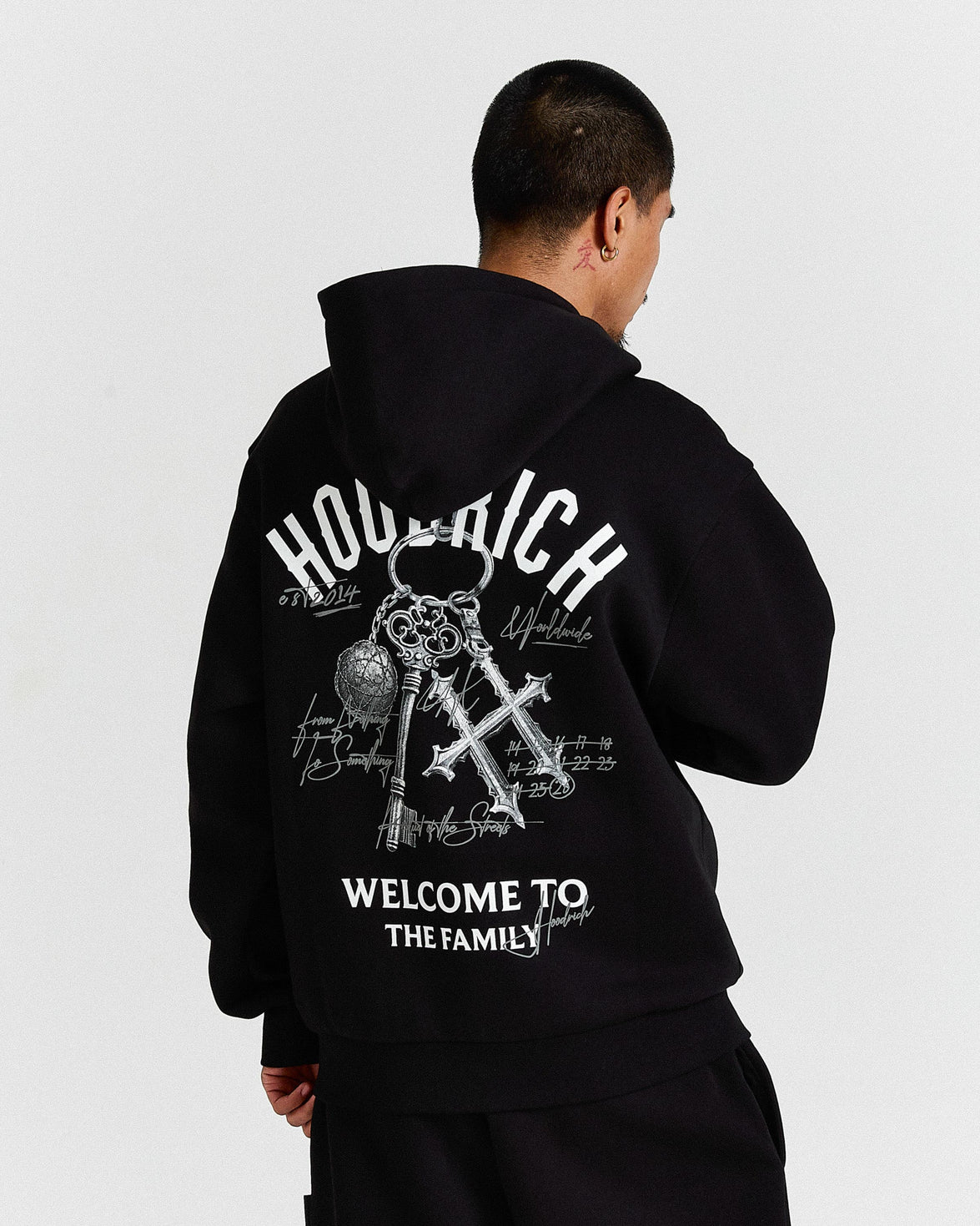 Person wearing a black hoodie with white text and graphics on the back, standing against a light gray background.