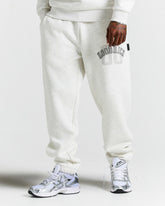 Person wearing light grey sweatpants with a brand logo and white sneakers on a white background