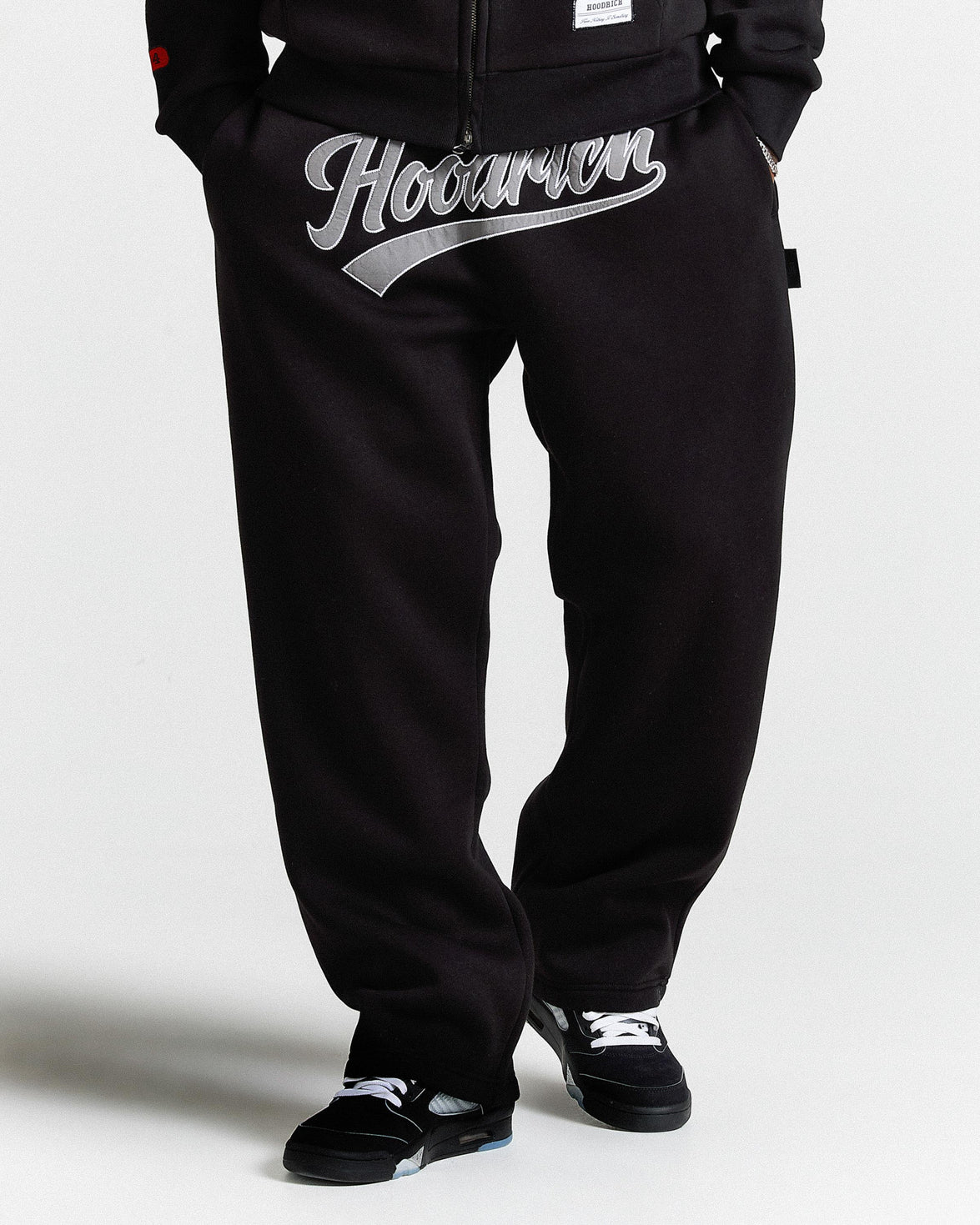 Black pants with 'Hoodrich' logo worn by a person on a white background