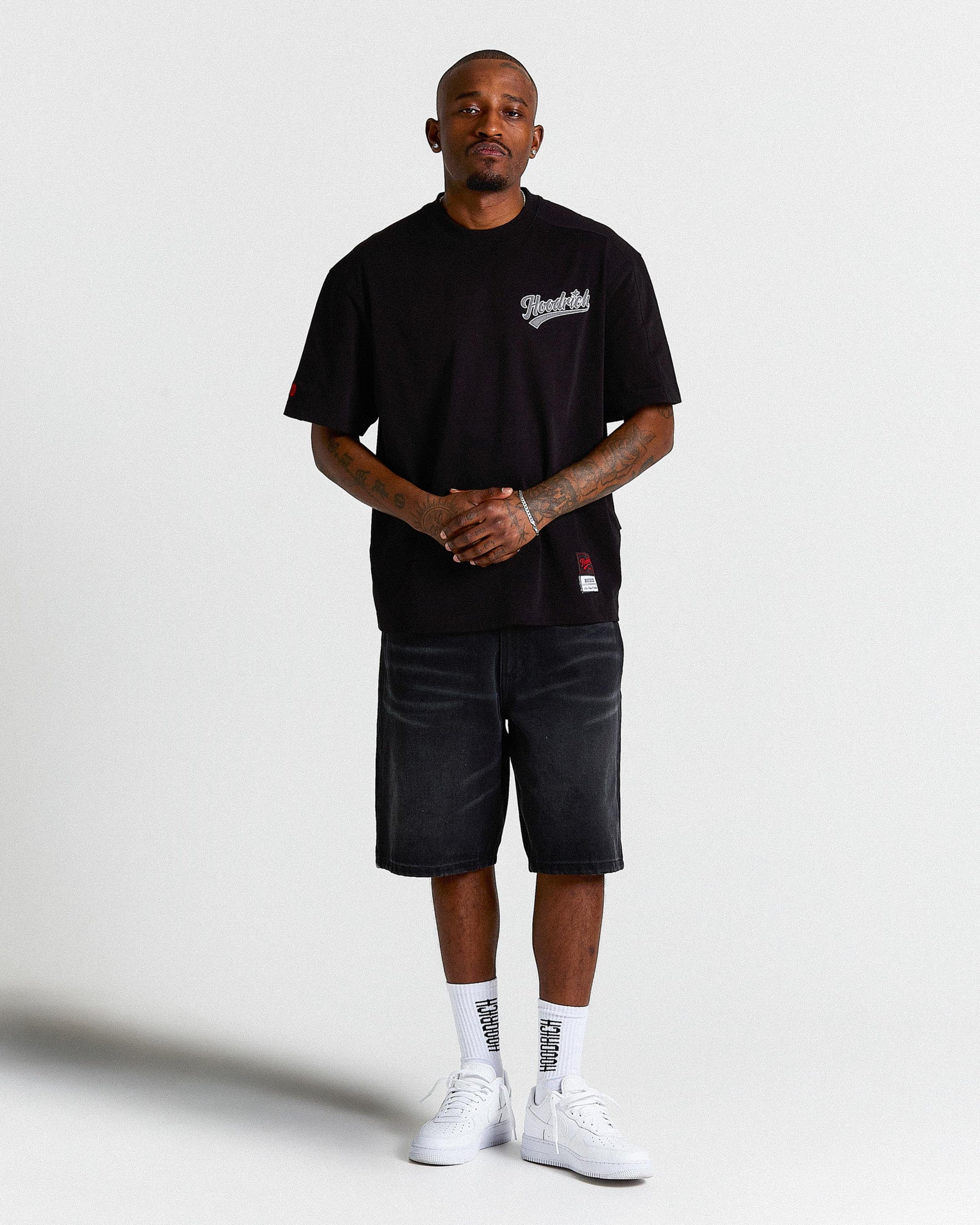 Man wearing a black t-shirt with a logo, black shorts, and white sneakers on a white background