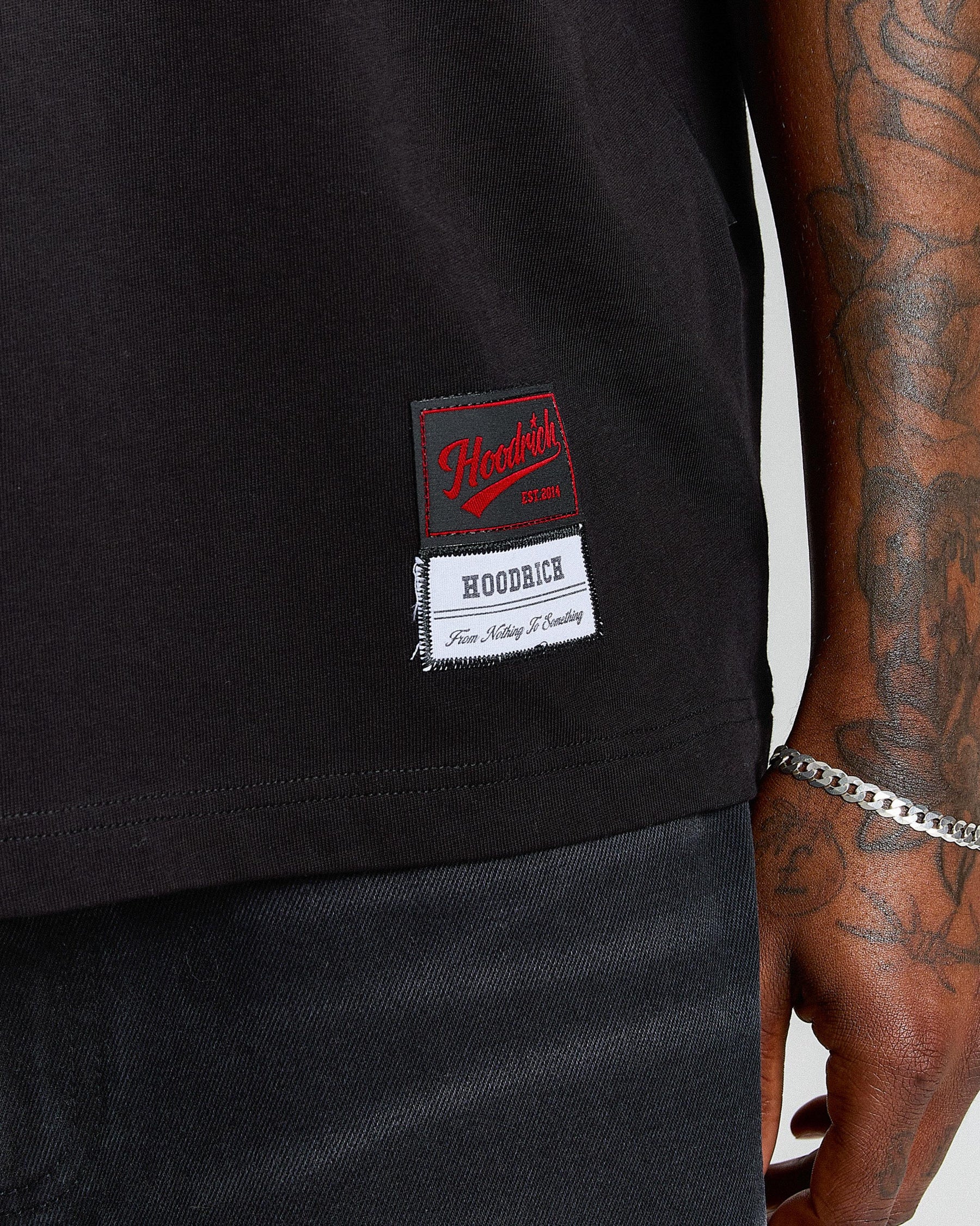 Black t-shirt with a visible brand label on a person wearing tattoos.
