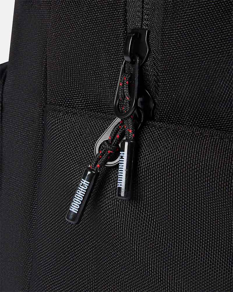 Close-up of a black woven fabric bag with a black zipper pull and a braided black-and-red zipper cord