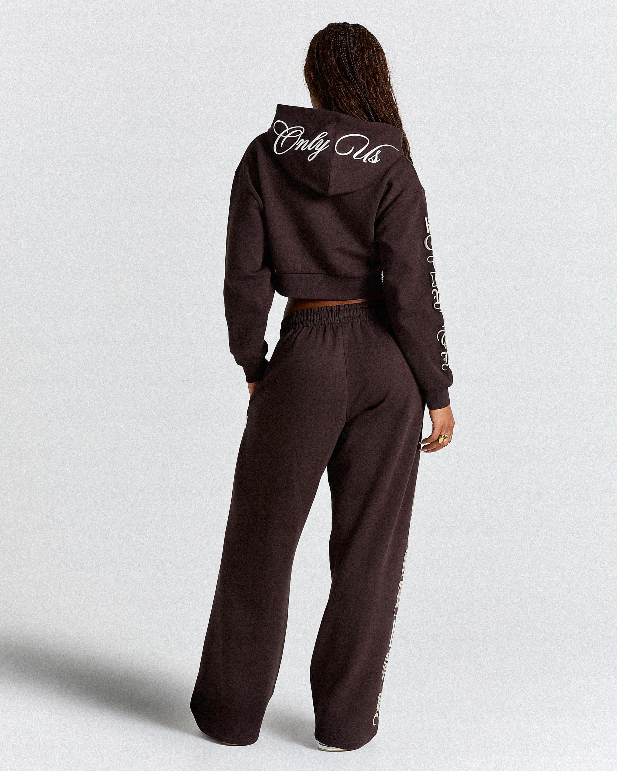 Person wearing a brown tracksuit with text on the back and sleeves against a white background