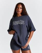 Woman wearing a navy oversized t-shirt with a logo on a light gray background