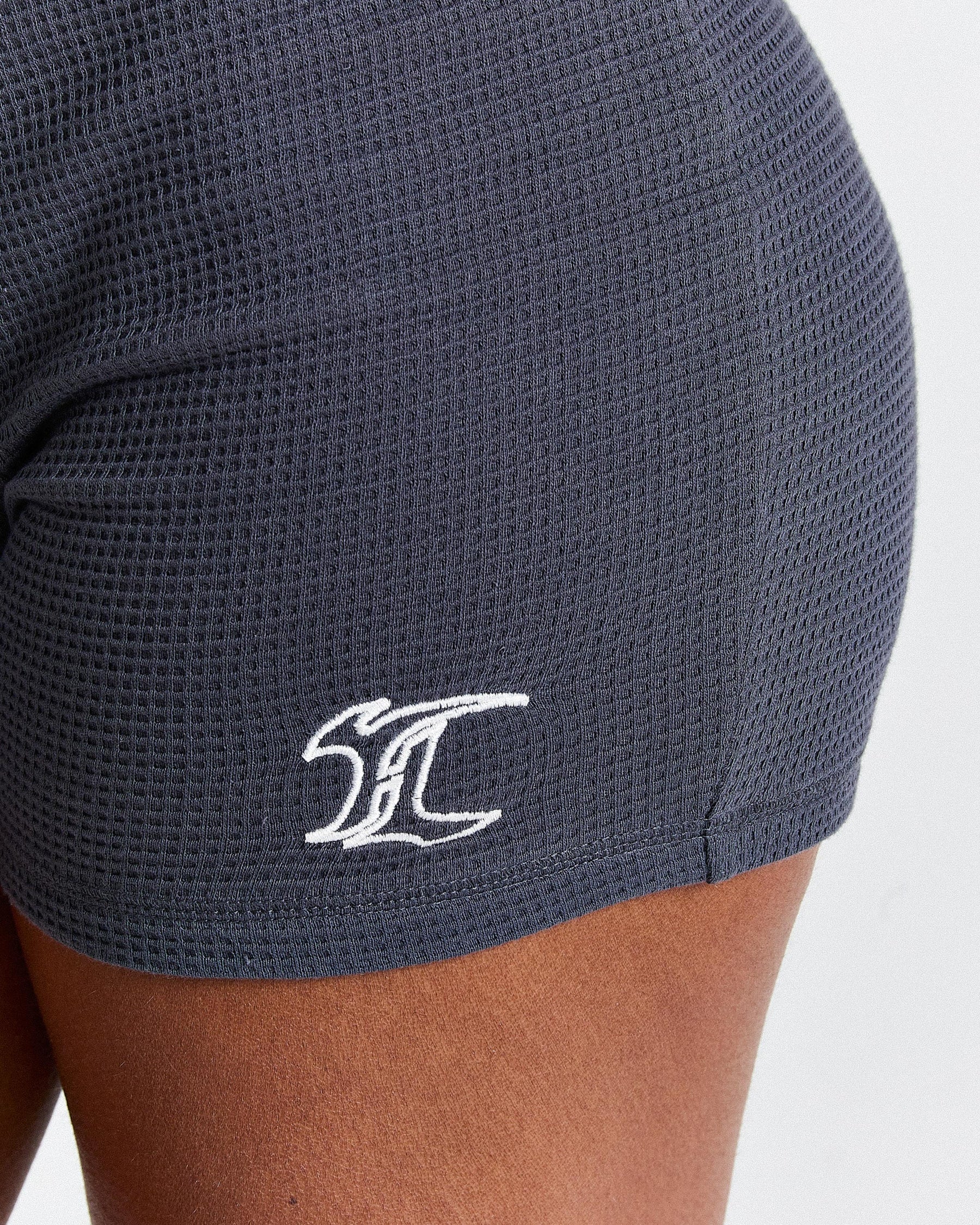 Dark gray athletic shorts with a white logo on a light gray background