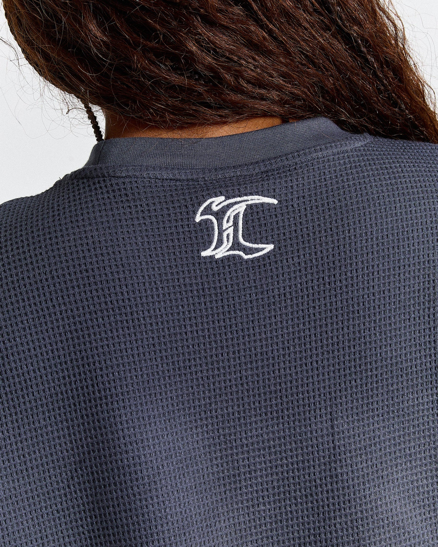 Navy blue textured shirt with a white logo on the back against a neutral background
