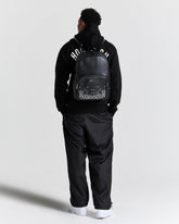 Person wearing a black tracksuit with a backpack on a white background
