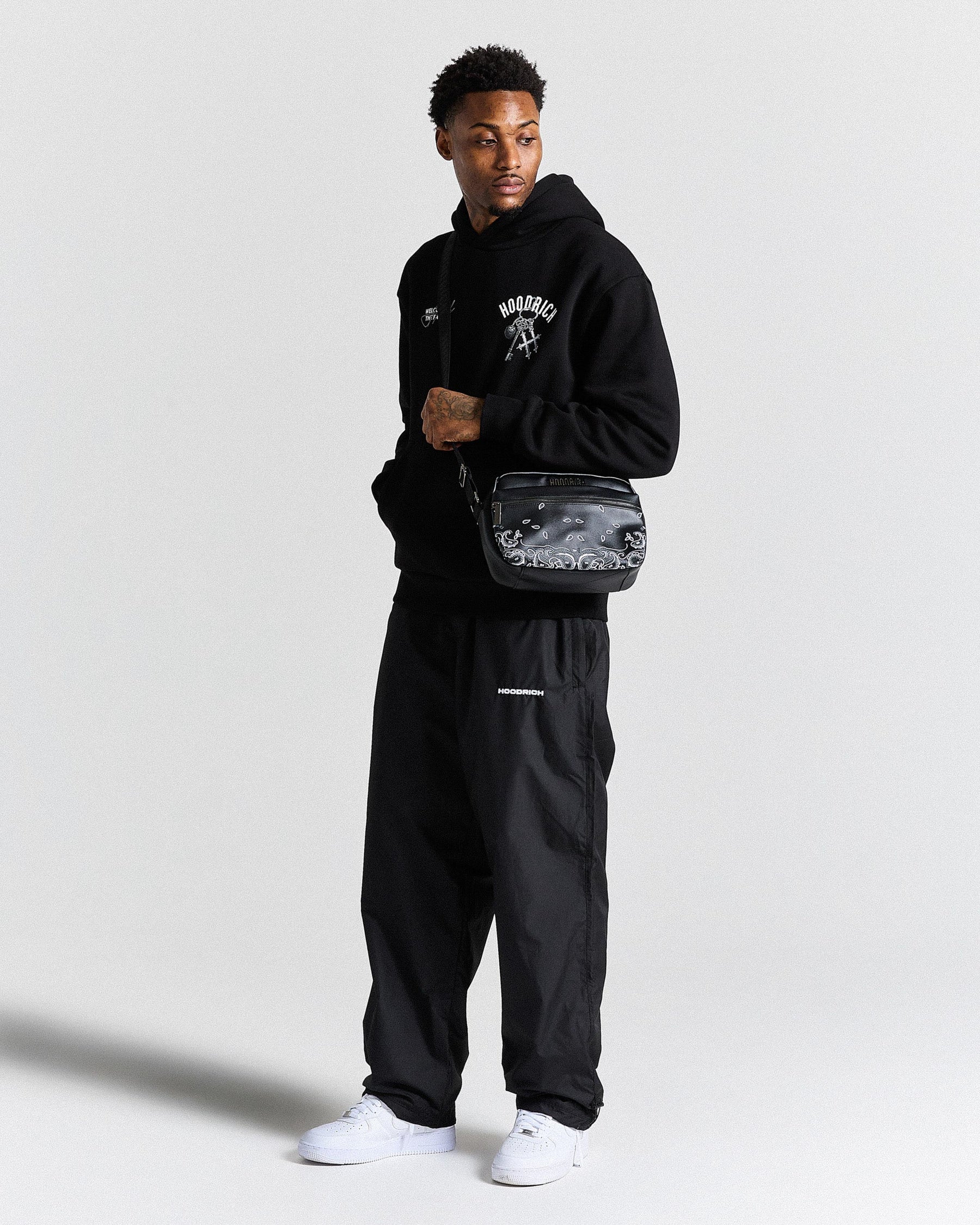 Person wearing a black hoodie and pants with a camouflage bag on a white background