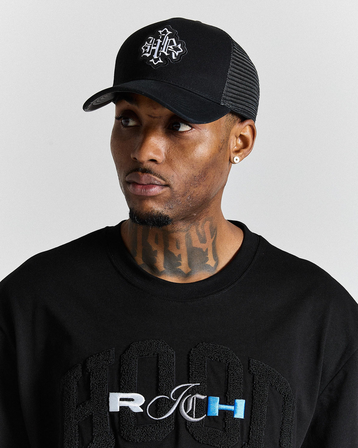 Man wearing a black cap and black shirt with visible branding on a gray background