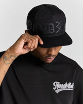 Person wearing a black cap and a black hoodie with 'Hoodrich' logo on a gray background
