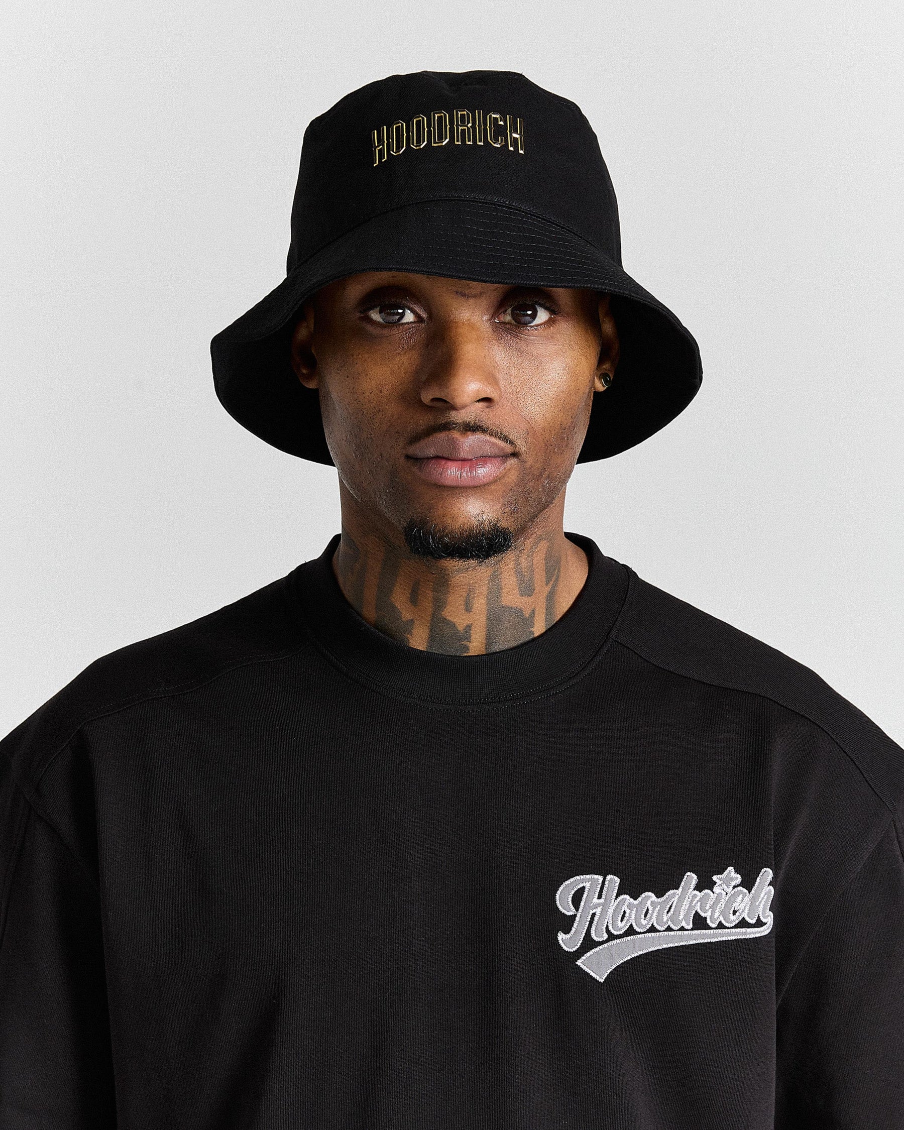 Person wearing a black 'Hoodrich' bucket hat and sweatshirt on a light gray background